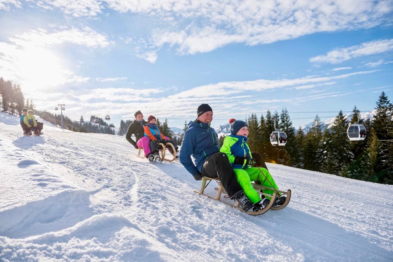 Eine Gruppe von Menschen rodeln auf einer verschneiten Piste an einem sonnigen Tag.