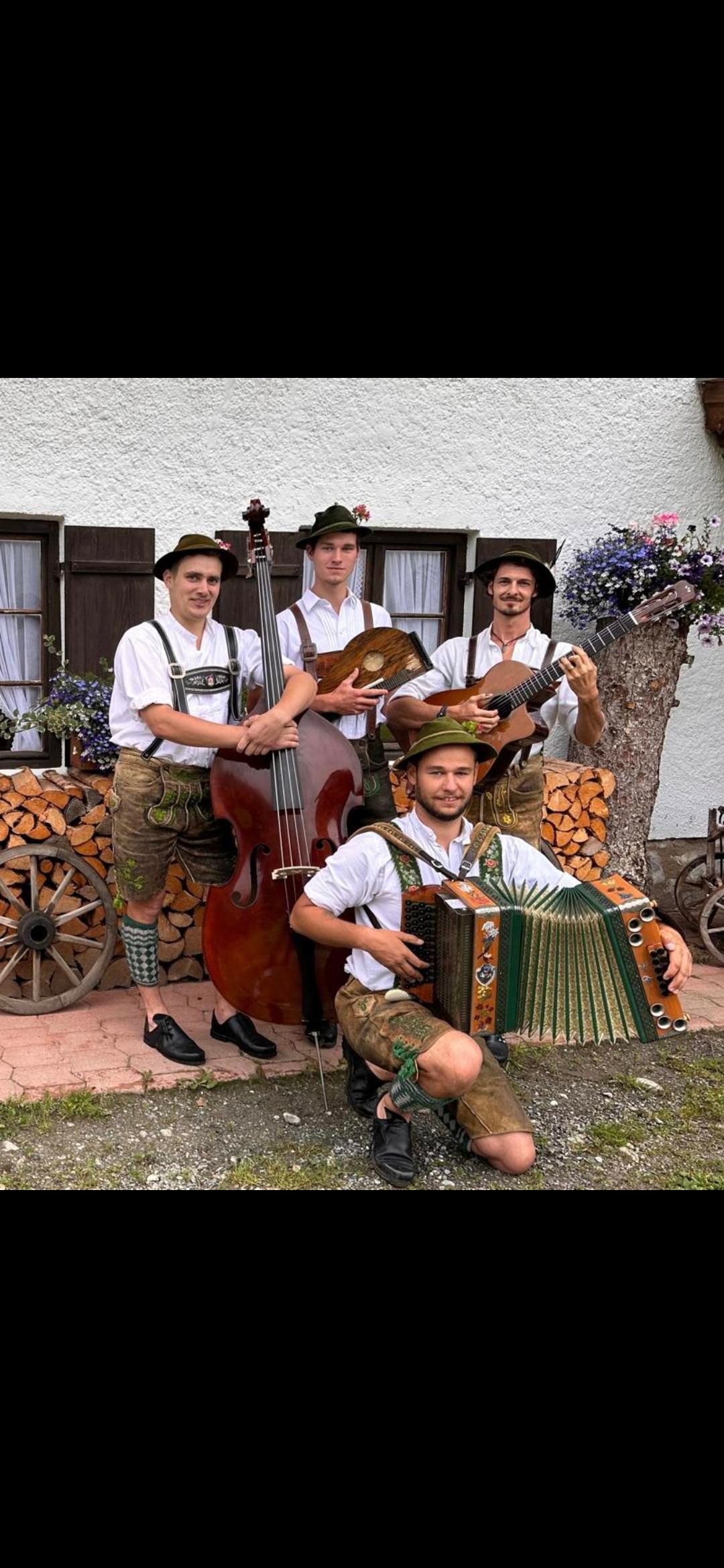Die vier Musikanten der Oimhittn Musi aus Oberbayern stehen mit ihren Instrumenten vor einem Haus.