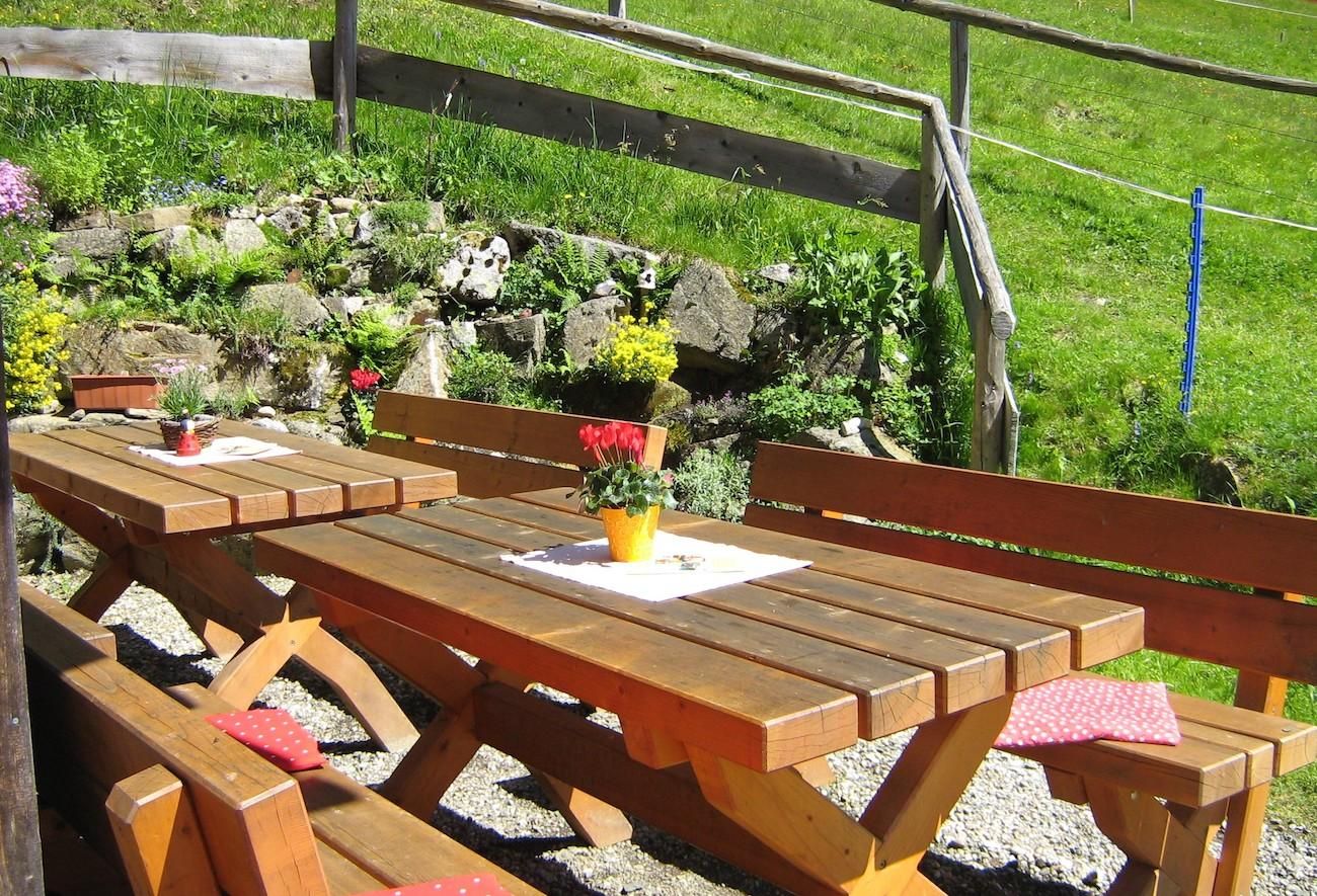 Terrasse der Alpe Bolgen in Bolsterlang, Holztische und Bänke im Freien.