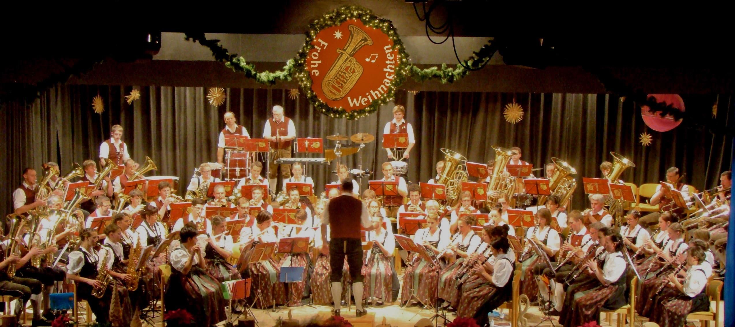 Ein großes Orchester in traditioneller bayerischer Tracht spielt auf einer Bühne.