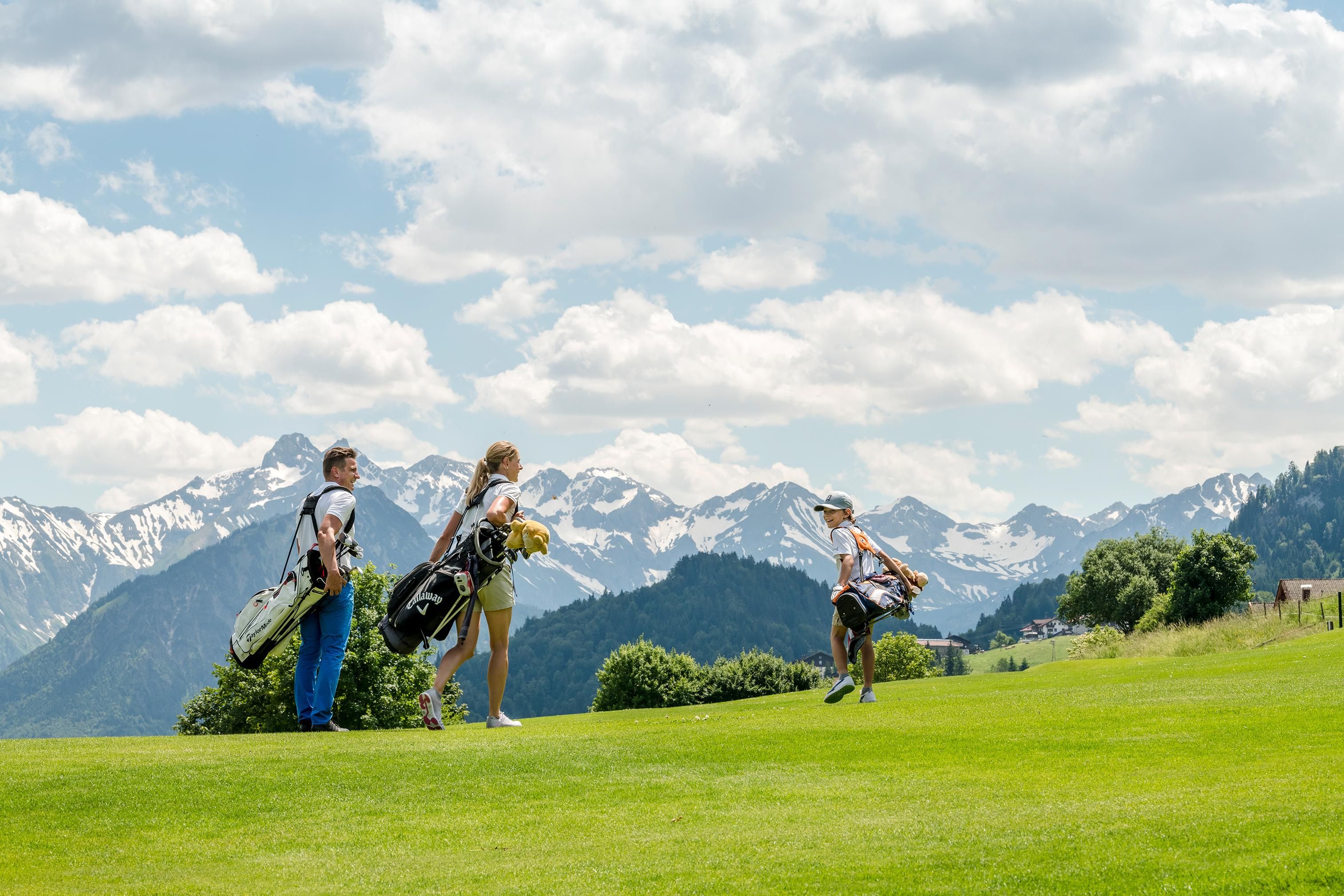 <p><p>Drei Golfer auf einem Golfplatz. Sie tragen Golftaschen und blicken in Richtung schneebedeckter Berge im Hintergrund.</p>