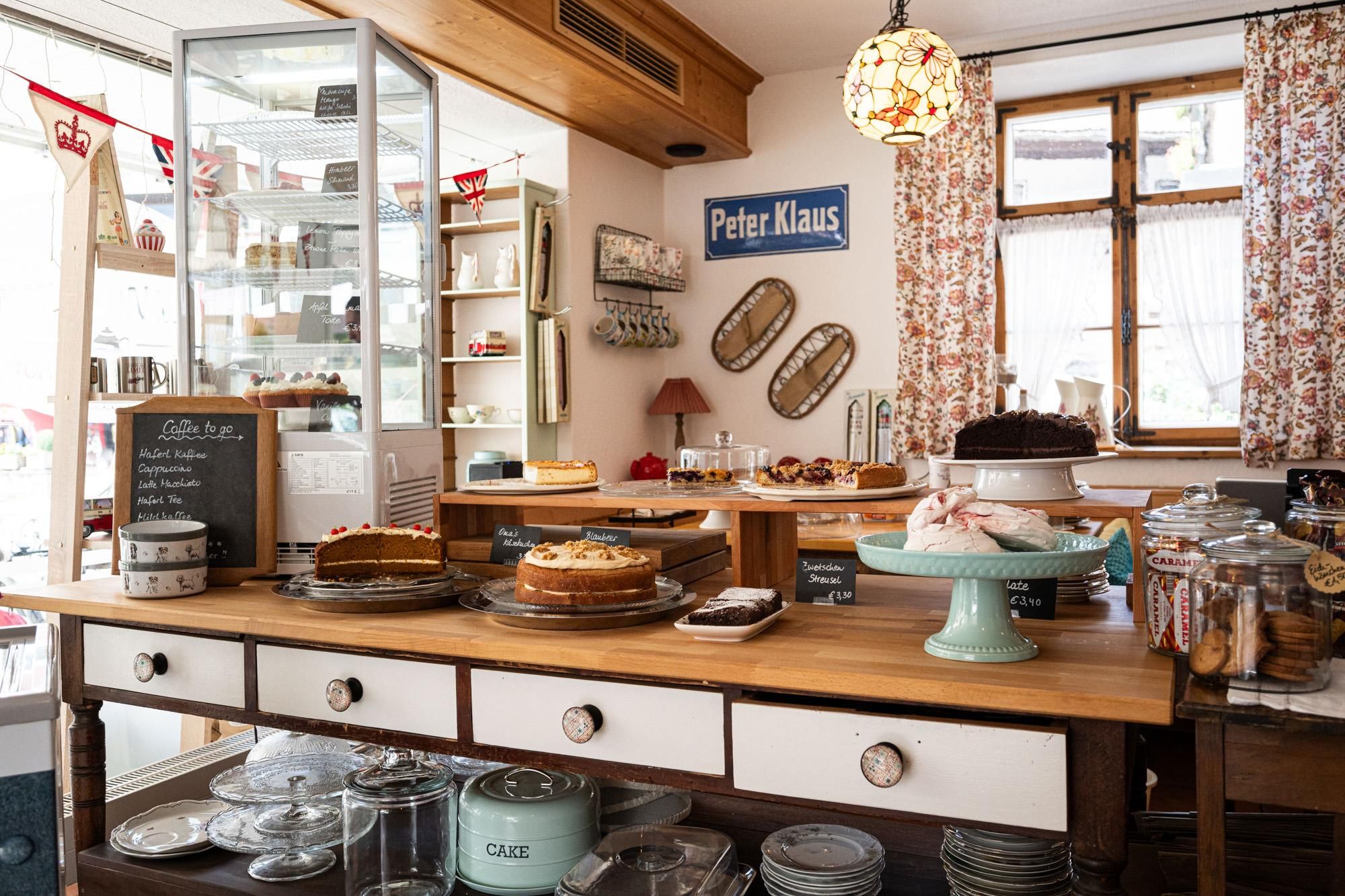 Ein Holztisch mit vier weißen Schubladen, darauf diverse selbsgebackene Kuchen und Torten, links eine weitere Kuchenvitrine.