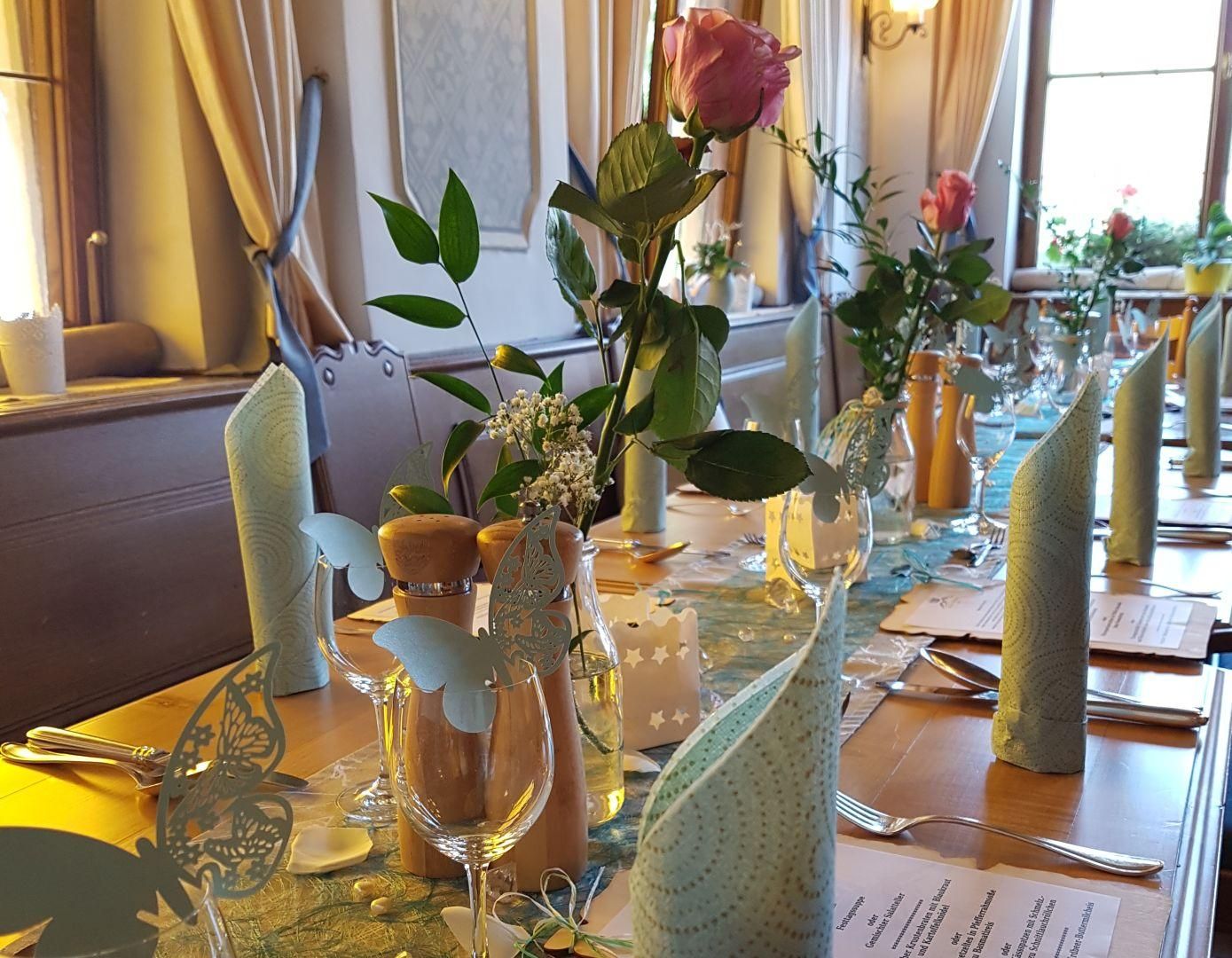 Ein schön gedeckter Tisch für eine größere Gruppe, mit hellgrünen Servietten und Rosen.