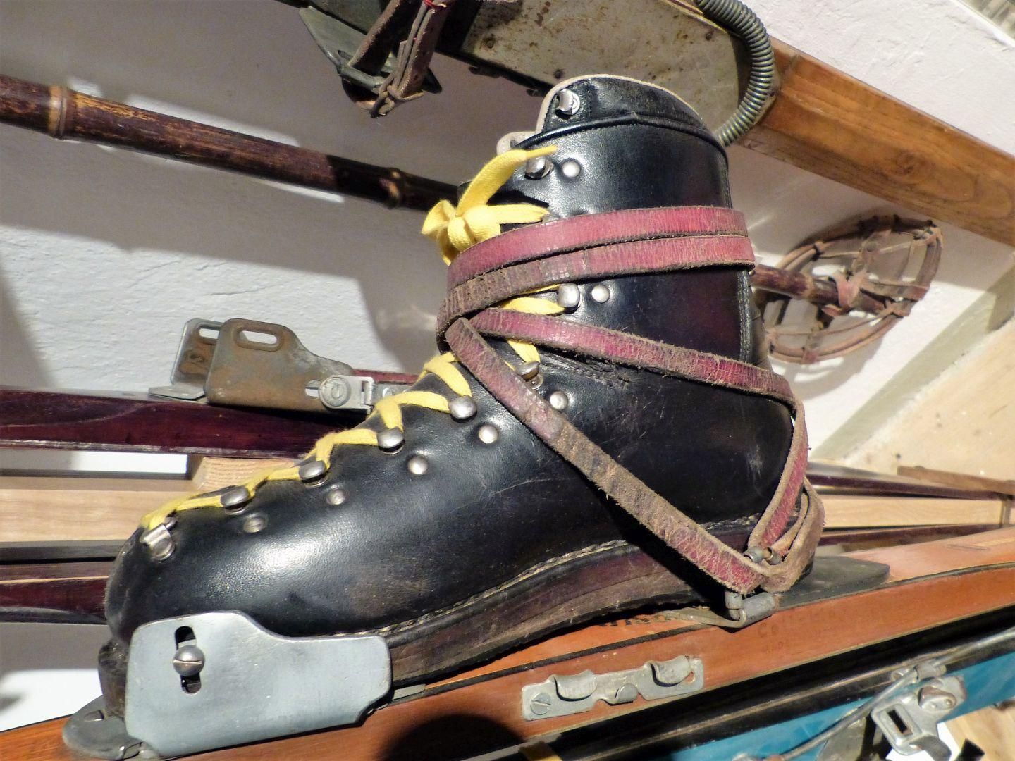Alter Leder-Skischuh mit Riemenbindung auf Holzski - ausgestellt im FIS-Skimuseum im Fischen