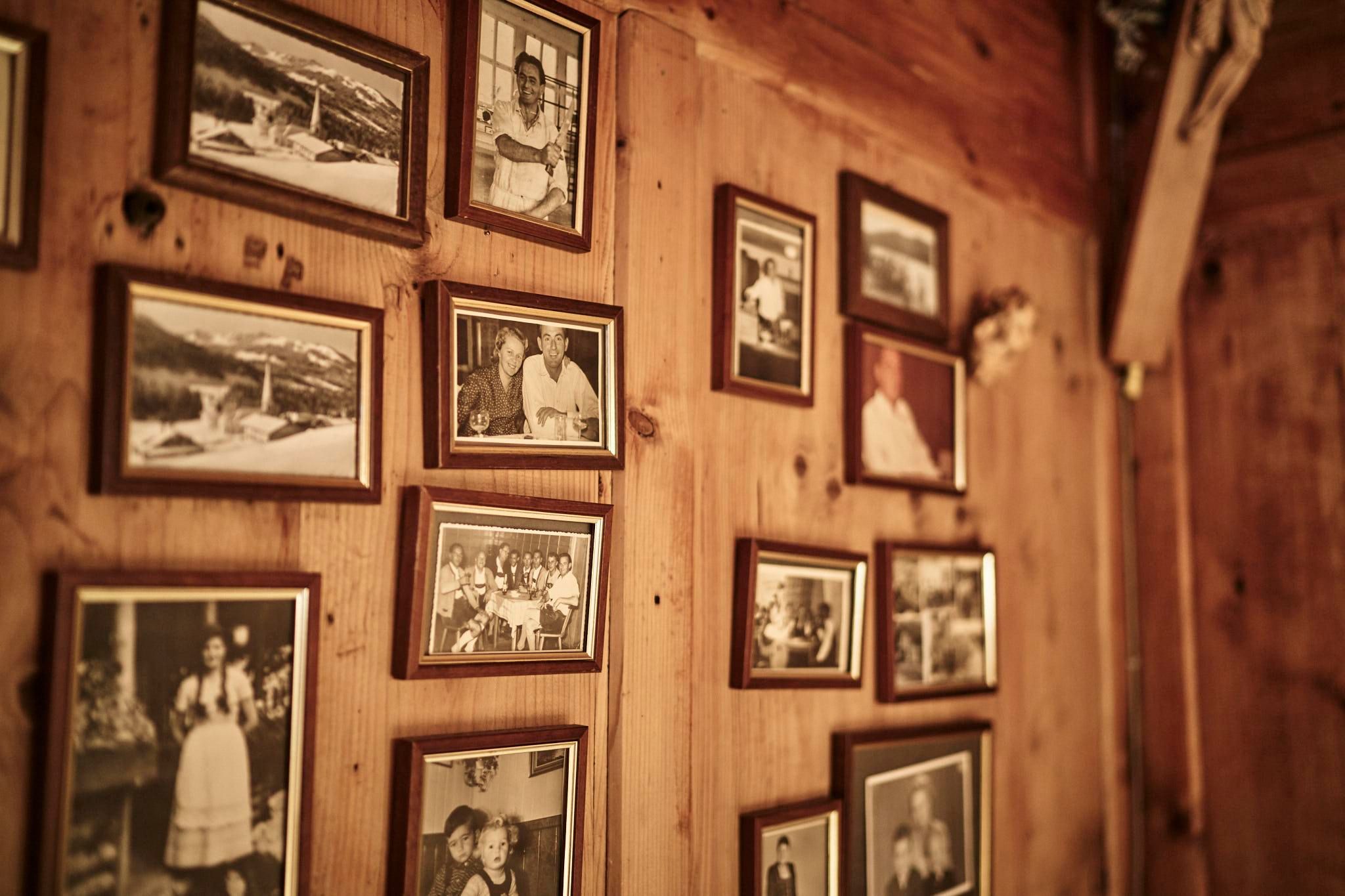 Holzwand dekoriert mit vielen gerahmten Schwarz-Weiß-Fotografien unterschiedlicher Größen. Warme, indirekte Beleuchtung.