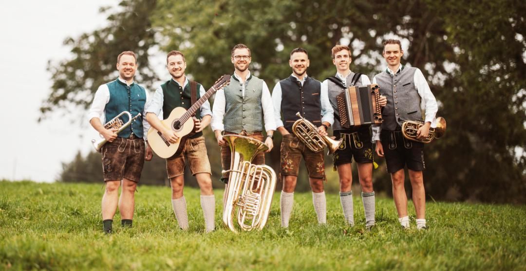 Die sechs Musikanten der Gruppe "Schlanzer" in Lederhose und Trachtenweste mit ihren Instrumenten Steirische Harmonika, Bariton, Trompete, Gitarre und Tuba.