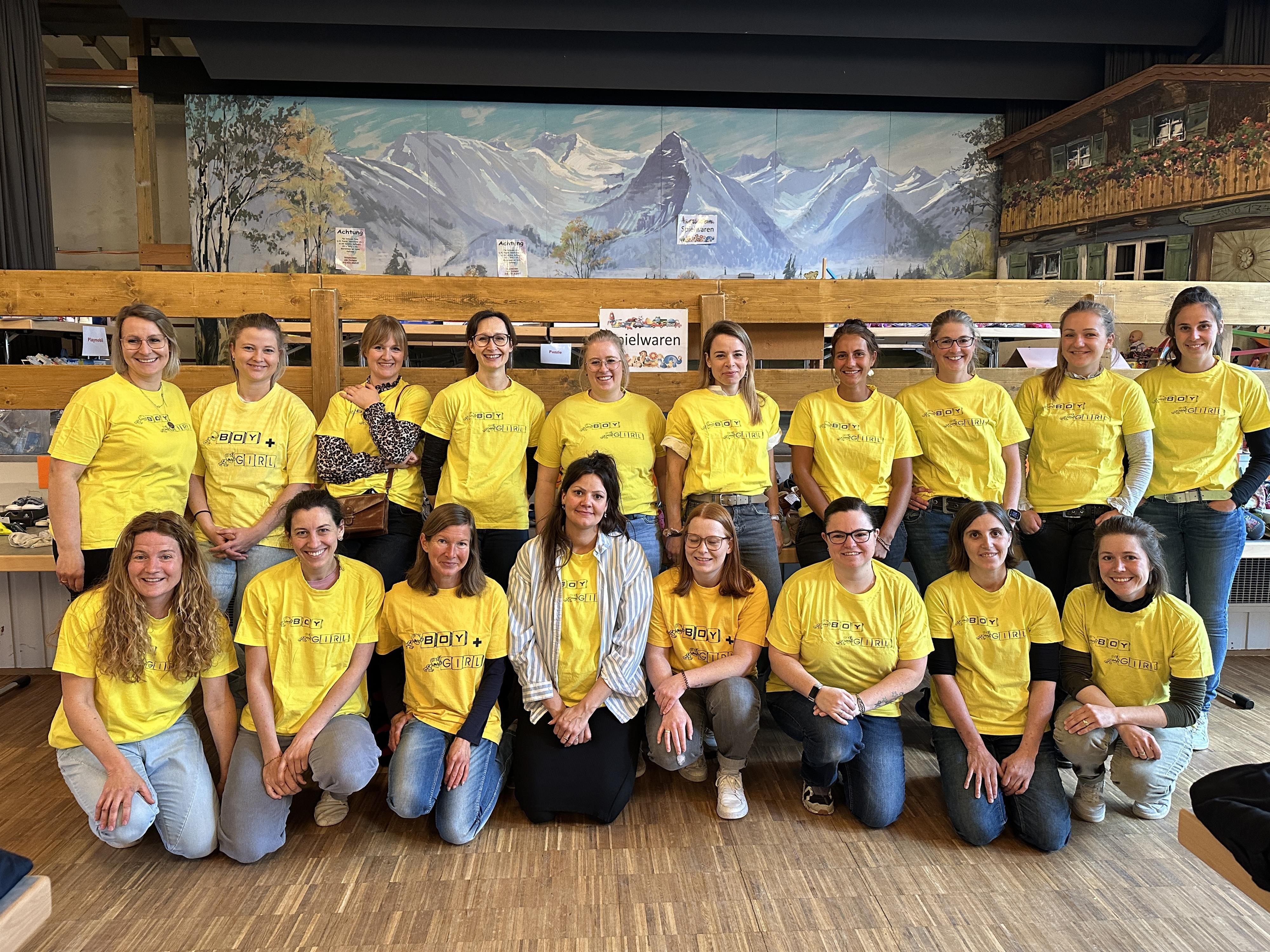 Gruppe von achtzehn lächelnden Frauen in gelben T-Shirts stehen in einer Halle