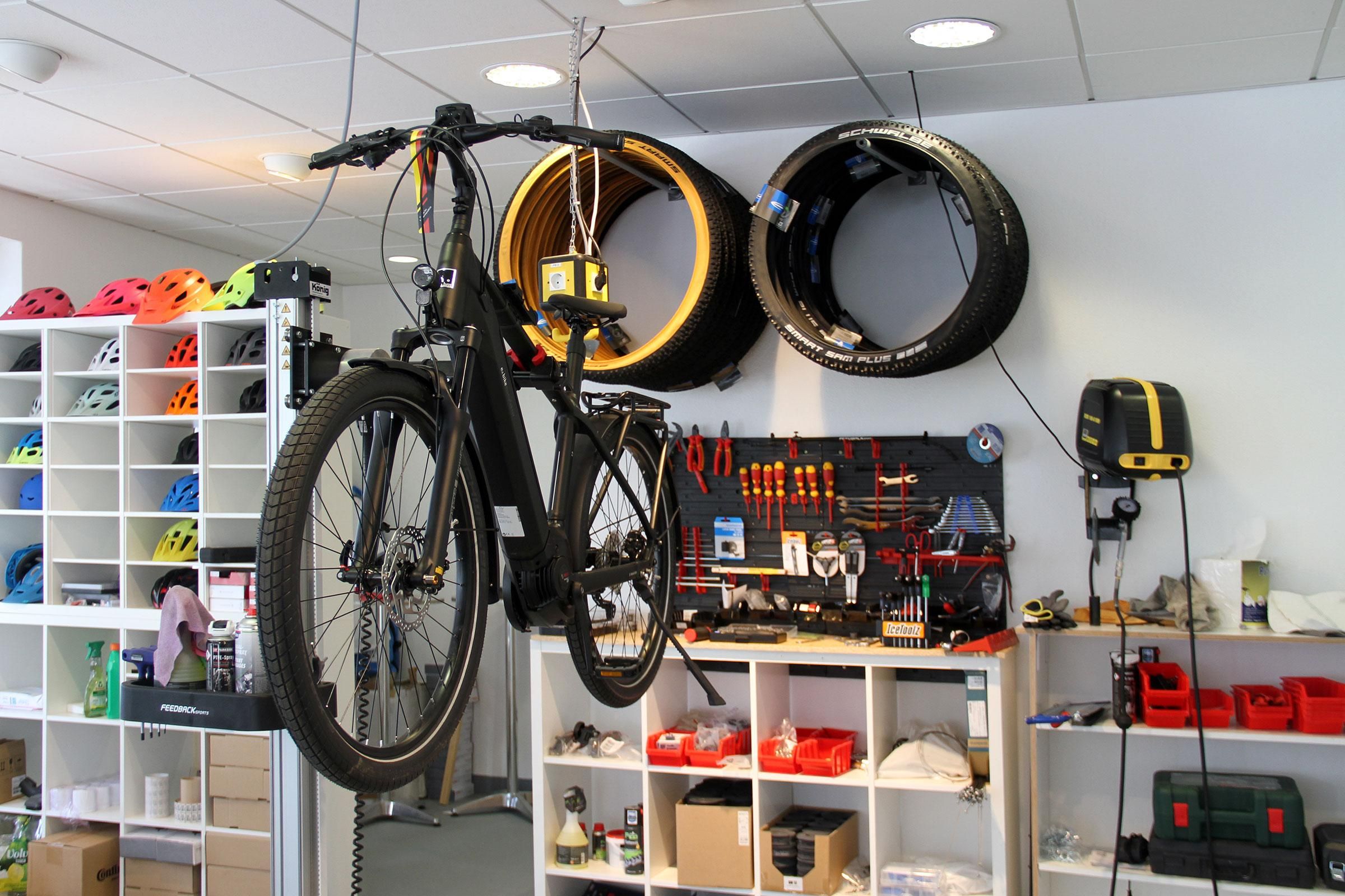 E-Bike hängt an der Decke, an Wand steht Regal mit Helmen, daneben hängen Fahrradreifen.