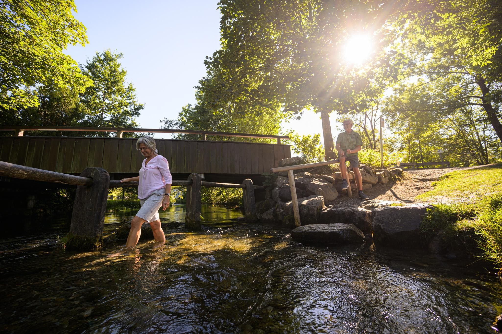 Eine Frau übt im Bach Wassertreten nach Pfarrer Kneipp, die Stelle ist über Treppen erreichbar.