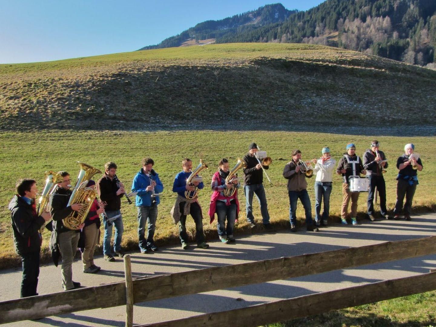 Eine Blaskapelle posiert für ein Gruppenfoto vor einer beeindruckenden Berglandschaft bei Sonnenschein.