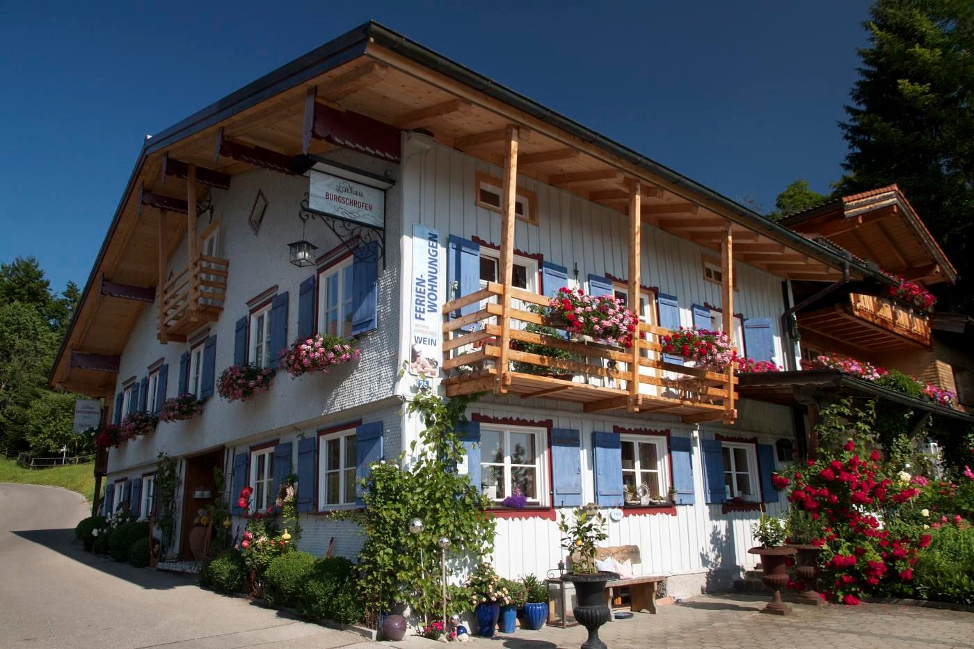 Blaue Fensterläden und rote Blumenkästen an den Fenstern. Holzbalkone mit roten Geranien.