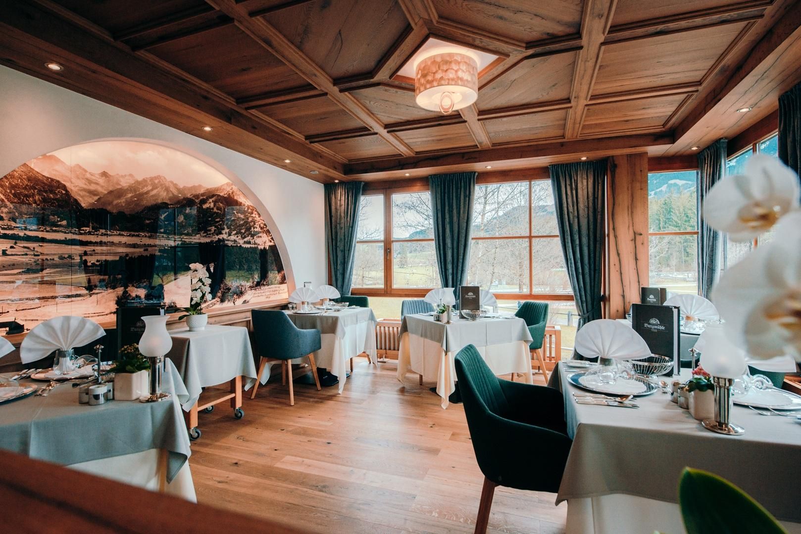 Die Alpenstube: die Decke besteht aus dunklem Holz, an der Wand links ein altes Bild von Bergen, große Fenster.