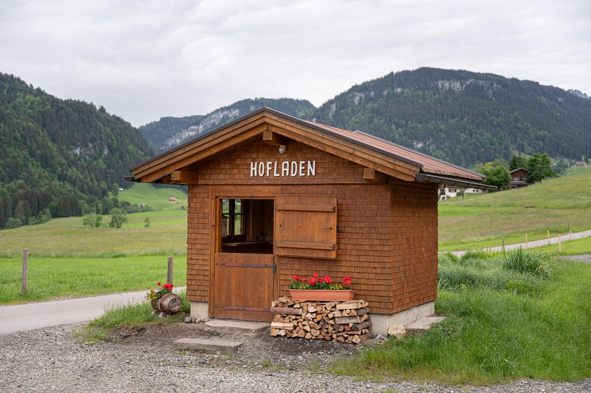 Der kleine Hofladen vom Naturgut Allgäu in Fischen-Maderhalm ist wie ein kleines Holzhaus gebaut mit Fenster, ein Holzstoß vor der Tür.
