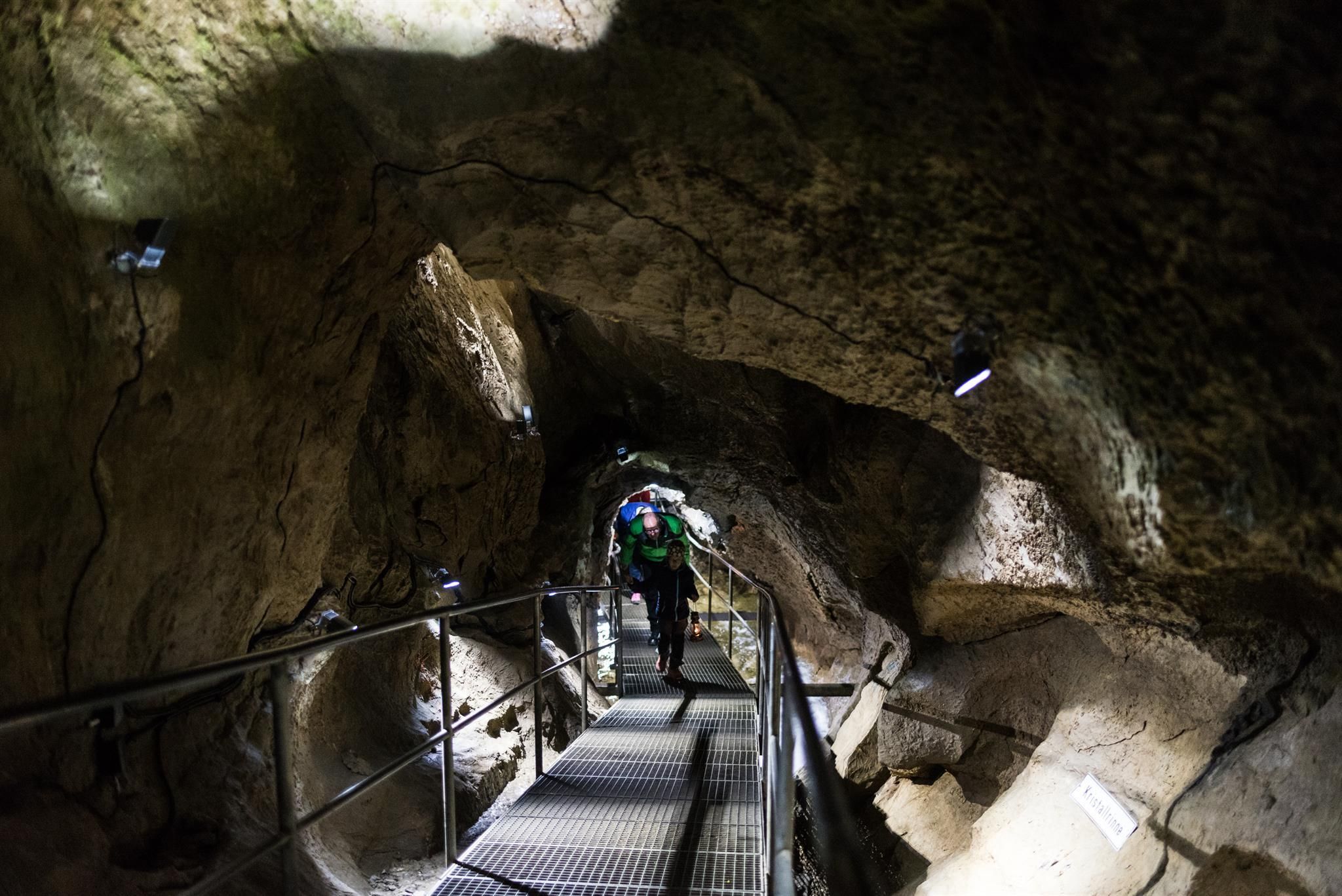 Metallgitterbrücke in einer dunklen Grotte. Rauhe, dunkle Felswände, graues Geländer.