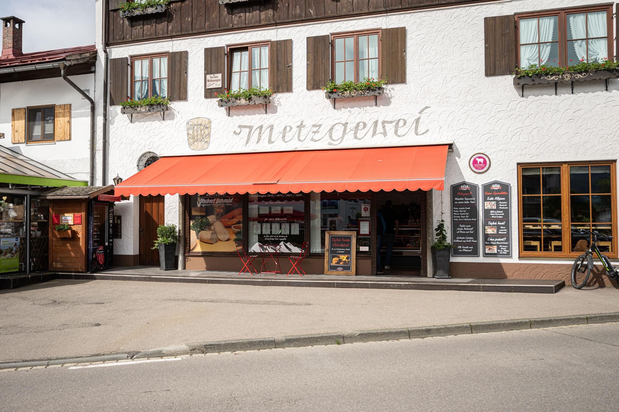 Eingang und Schaufenster der Metzgerei Schmid in Fischen, eine orangefarbene Markise ist ausgefahren.