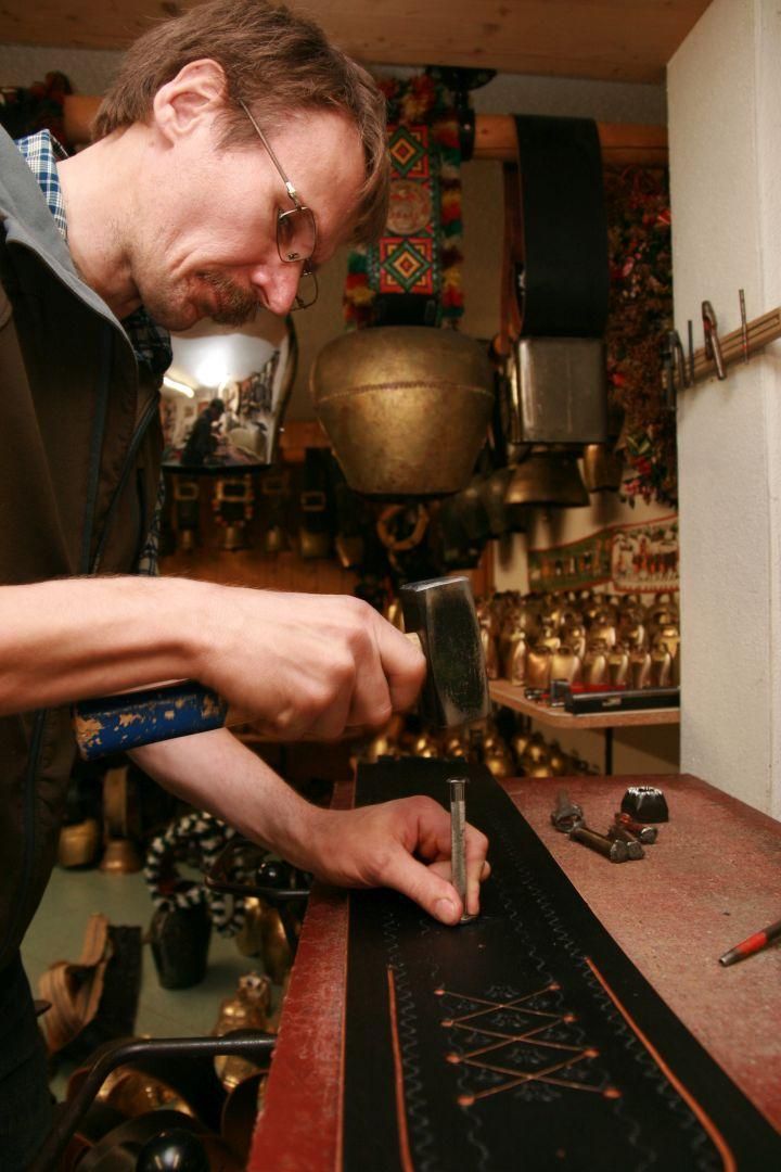 Ein Mann mit Brille und Schnurrbart arbeitet an einem dunklen Lederriemen mit hellen Verzierungen.