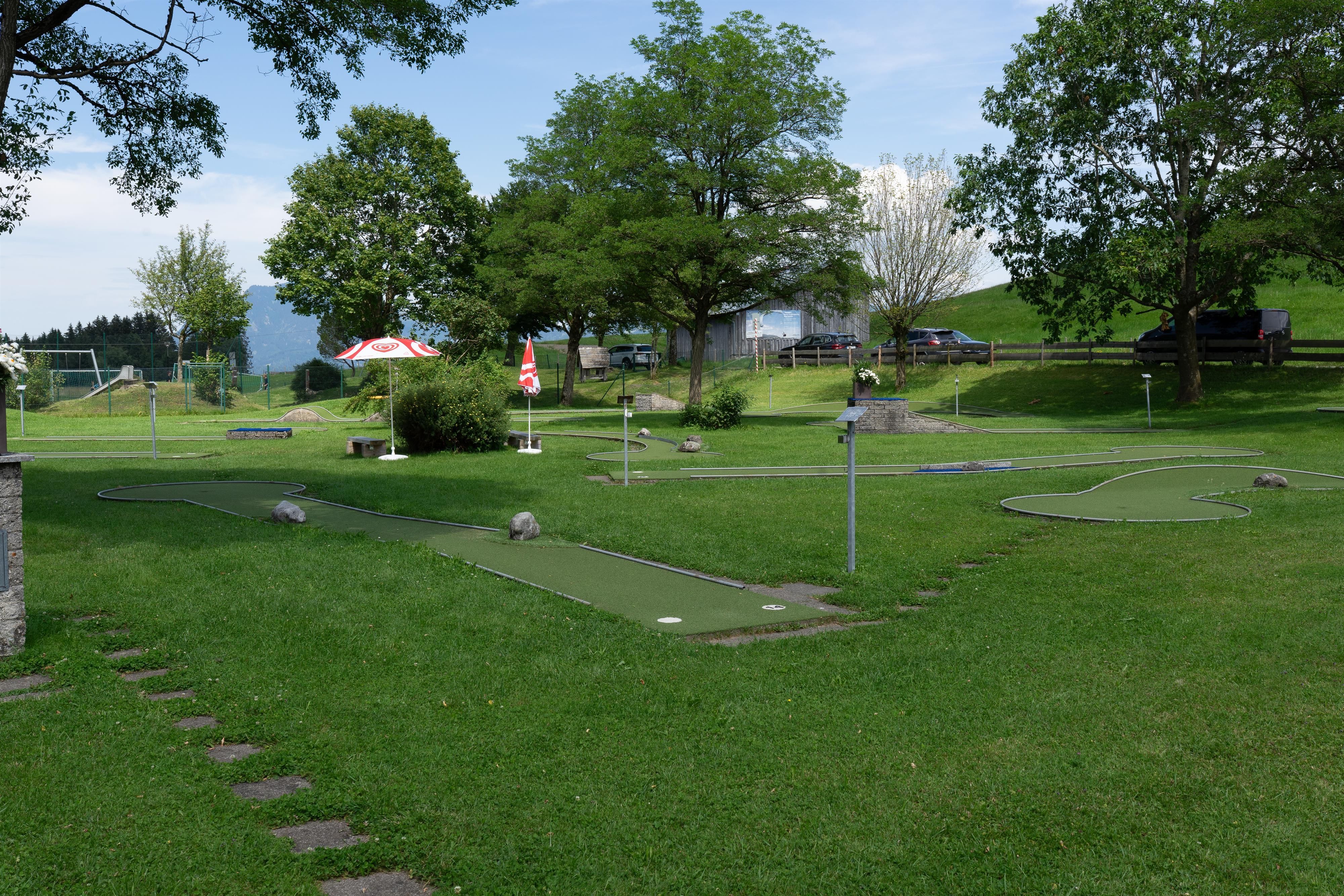 Ein weitläufiger Minigolfplatz mit mehreren grünen Bahnen, eingebettet in eine gepflegte Grünfläche mit Bäumen und Sträuchern.
