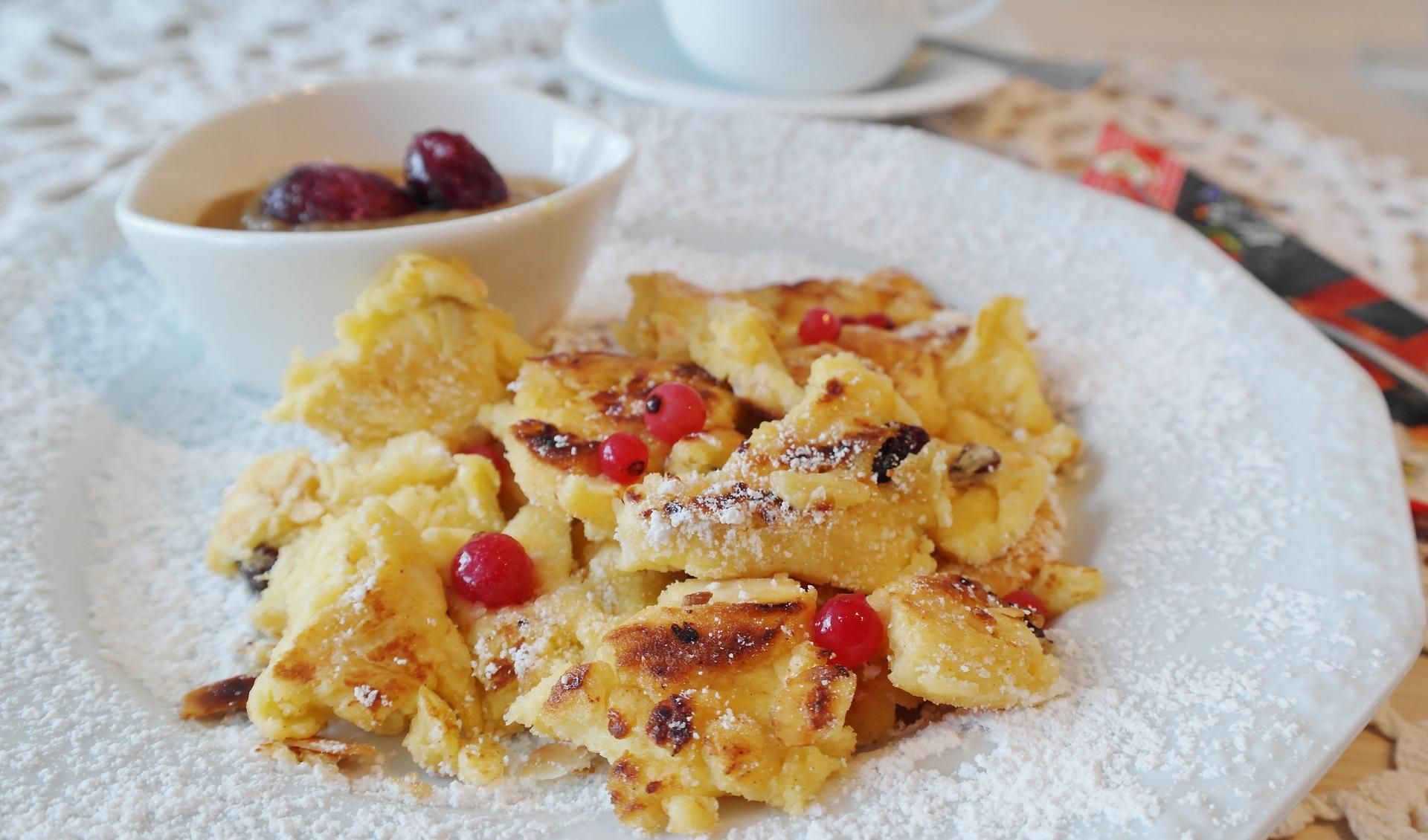 Kaiserschmarrn auf einem weißen Teller angerichtet mit einer Kompottschüssel.