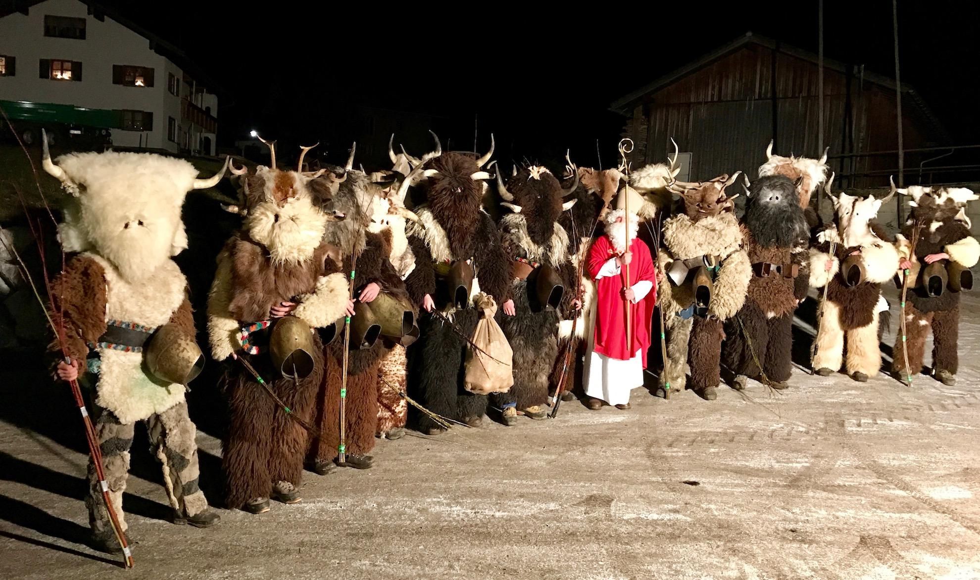 Gruppe maskierter Klausen und ein Bischof stehen nachts im Freien.