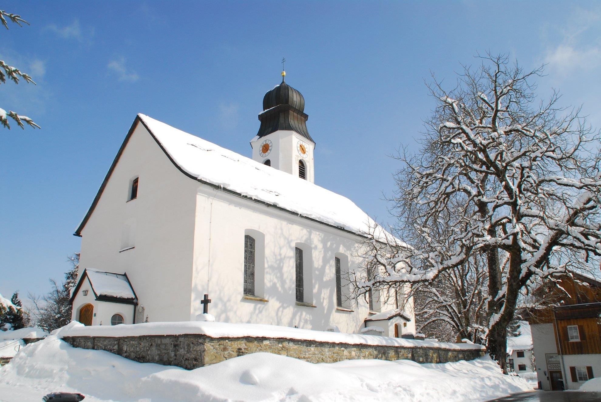 Verschneite Kirche mit großen Fenstern an der Seite. Glockenturm mit schwarzen Dach.