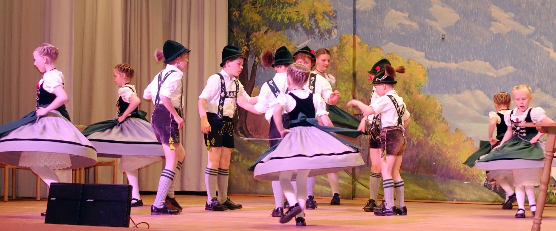 Mädchen und Jungen in Tracht auf der Bühne, sie führen einen traditionellen Tanz auf.