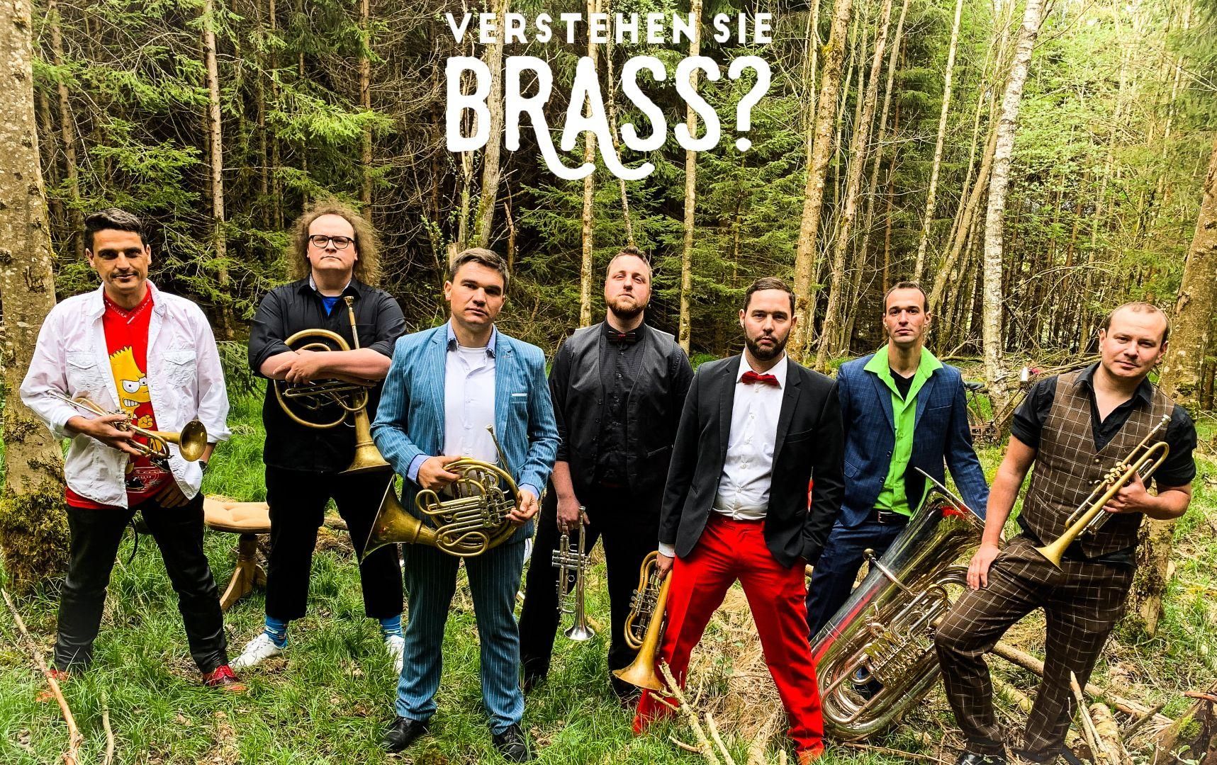 Die siebenköpige Band "Verstehen Sie Brass?" steht auf einer Waldlichtung, jedes Mitglied mit seinem Insturment.