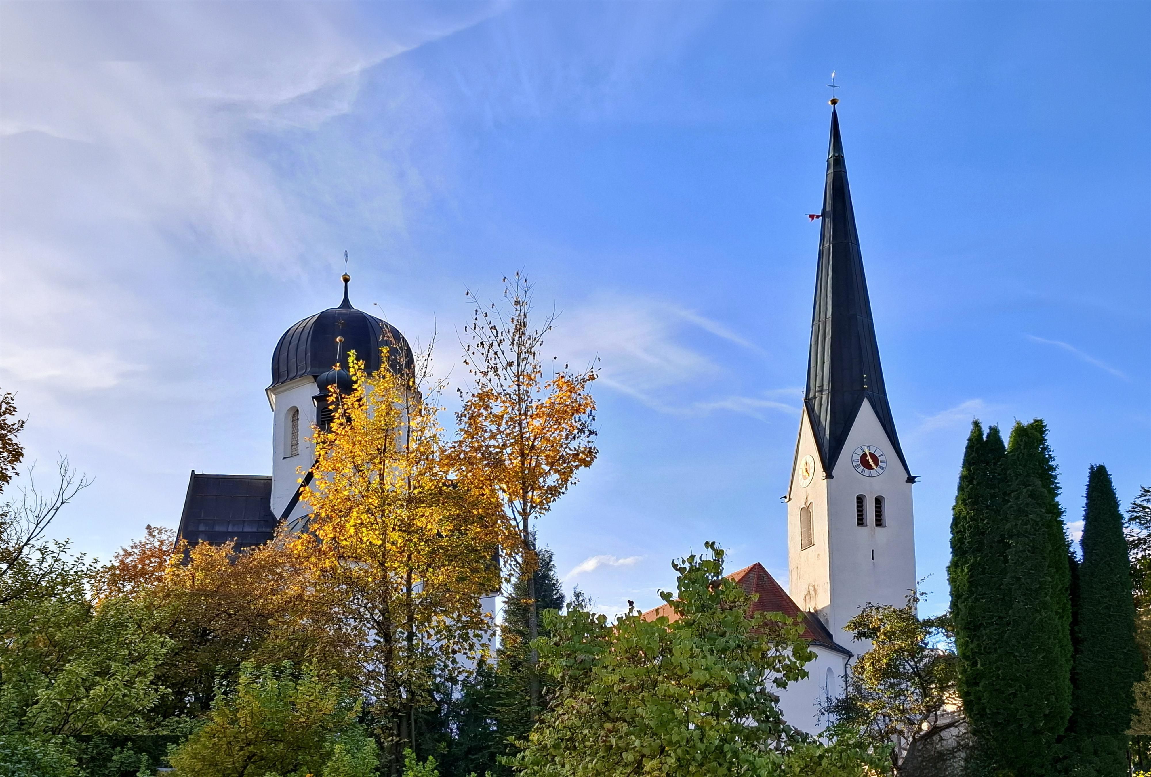Der Kirchturm der 900 Jahre alten Pfarrkirche St. Verena ragt in den wolkenlosen, blauen Himmel hinauf. Daneben von Laubbäumen umrahmt steht die Kuppel der schönen Frauenkapelle welche zusammen mit der Kirche, eingebunden in den Friedhof zusammen zu einer optischen Schönheit verschmelzen.