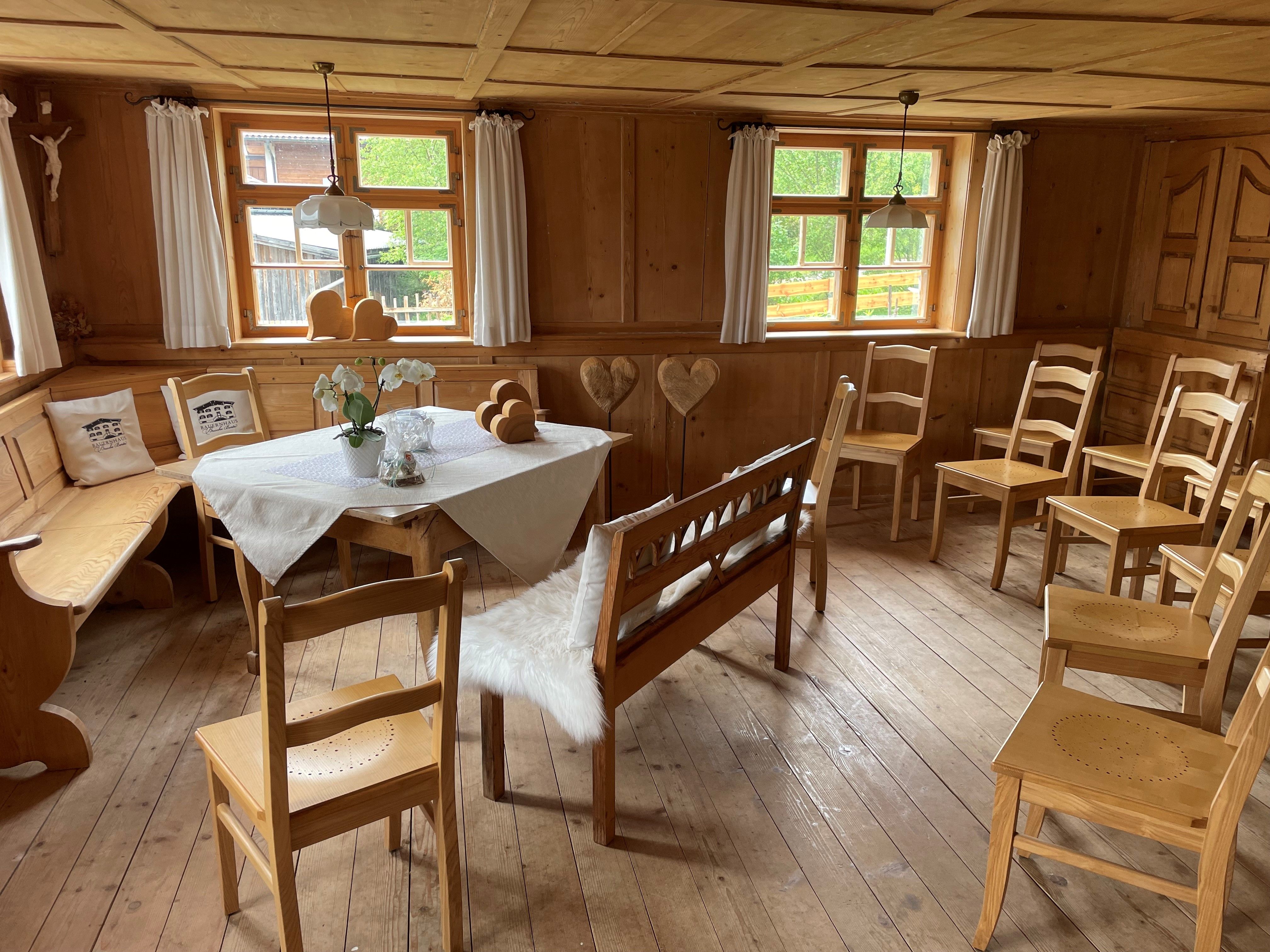 Bauernstube mit Holzboden und -wänden. Dekorierter Trautisch mit Tischdecke, Stühlen und Bänken. Fenster mit Vorhängen.