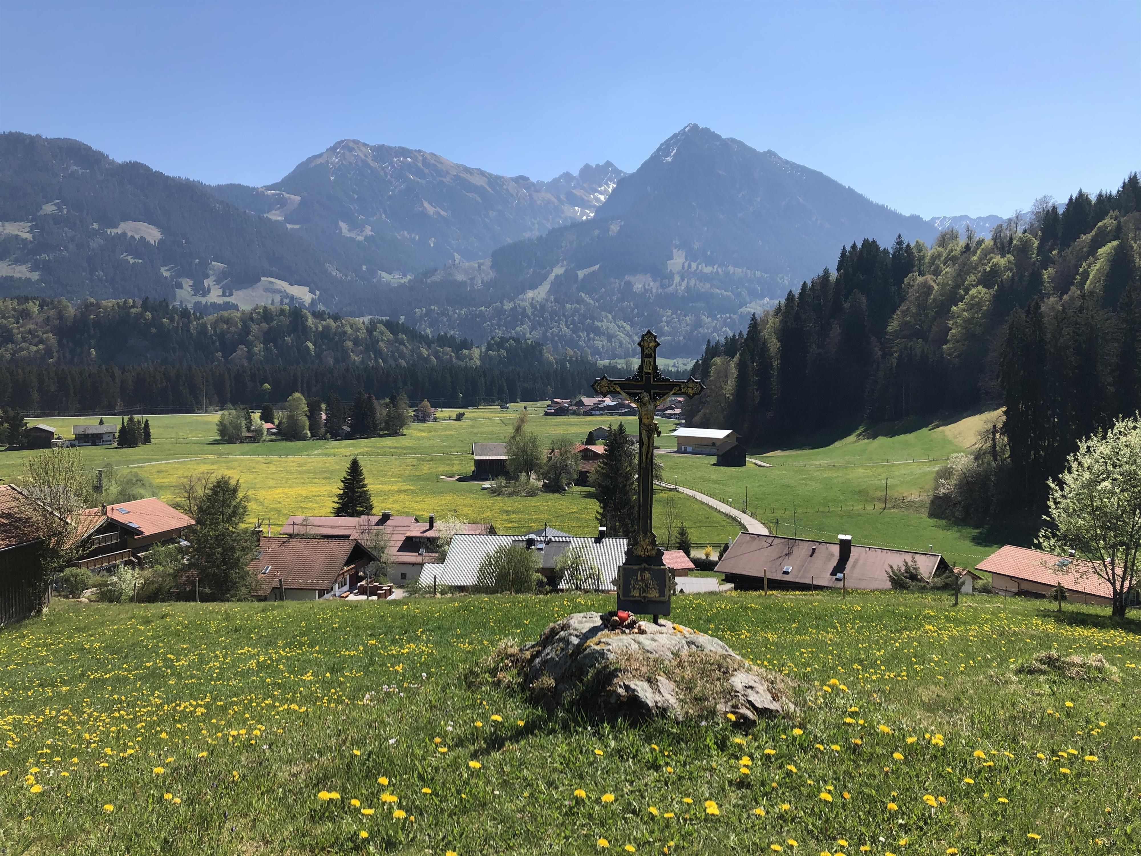 Ein schwarzes Wegkreuz oberhalb vom Ortsteil Fischen-Langenwang, auf der anderen Talseite ein fast 2000 m hoher Berg