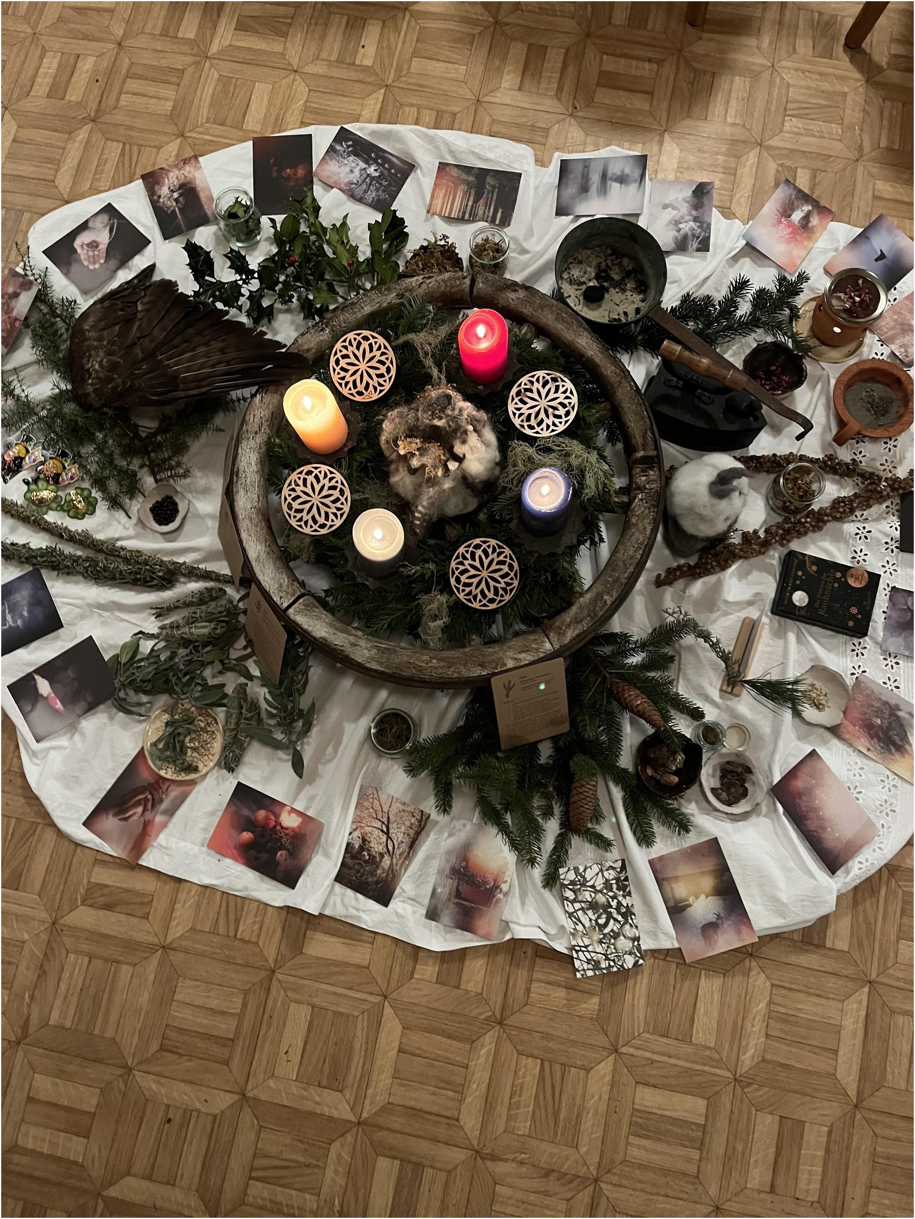 Weißes Tuch mit Kerzen, Holzscheibe, Pflanzen und Symbolkarten, kreisförmig auf Parkettboden angeordnet.