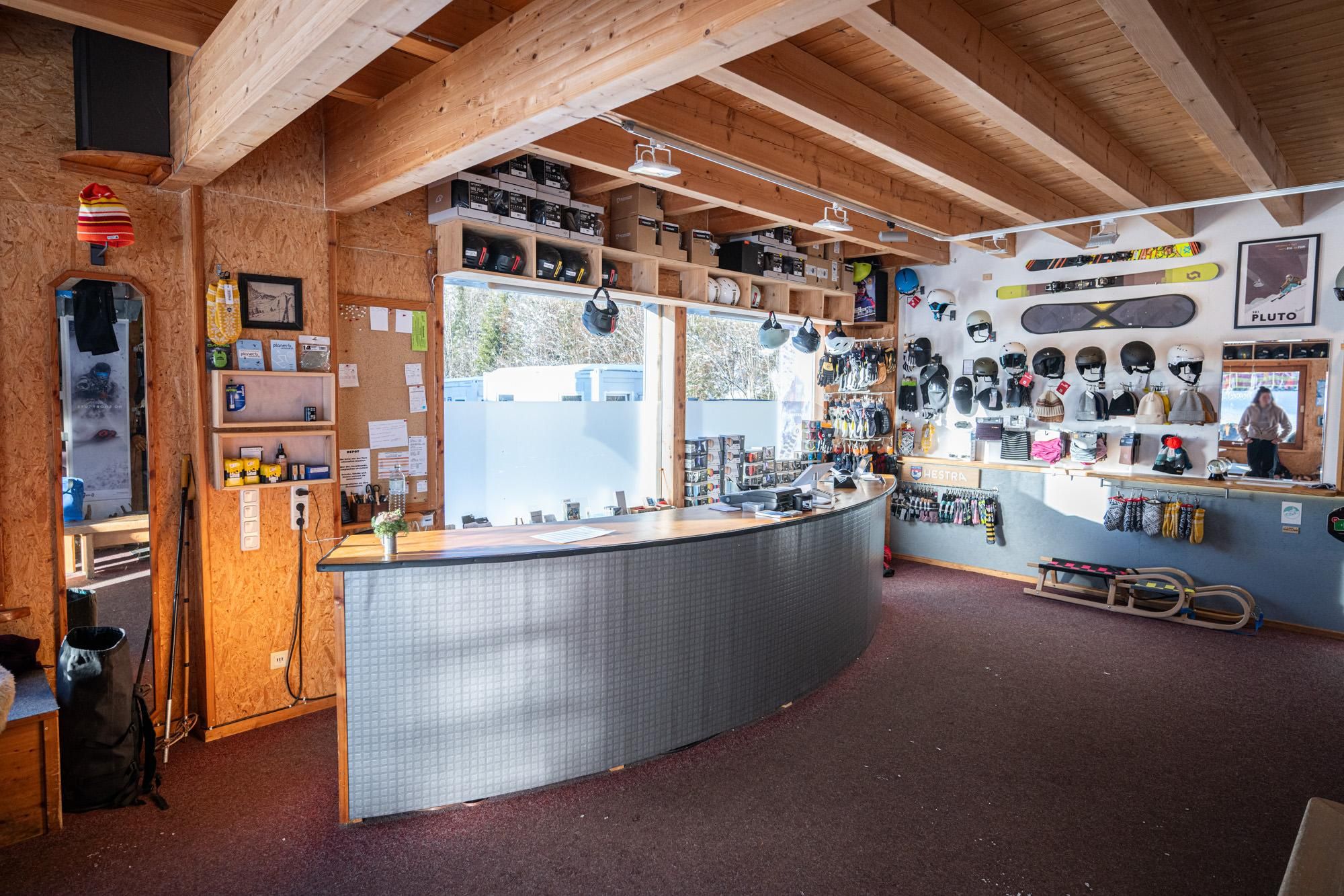 Innenansicht Planet B Wintersport: Theke, Regale mit Helmen, Schuhen, Boards. Schlitten, Stöcke. Helle Beleuchtung, Holzbalken.