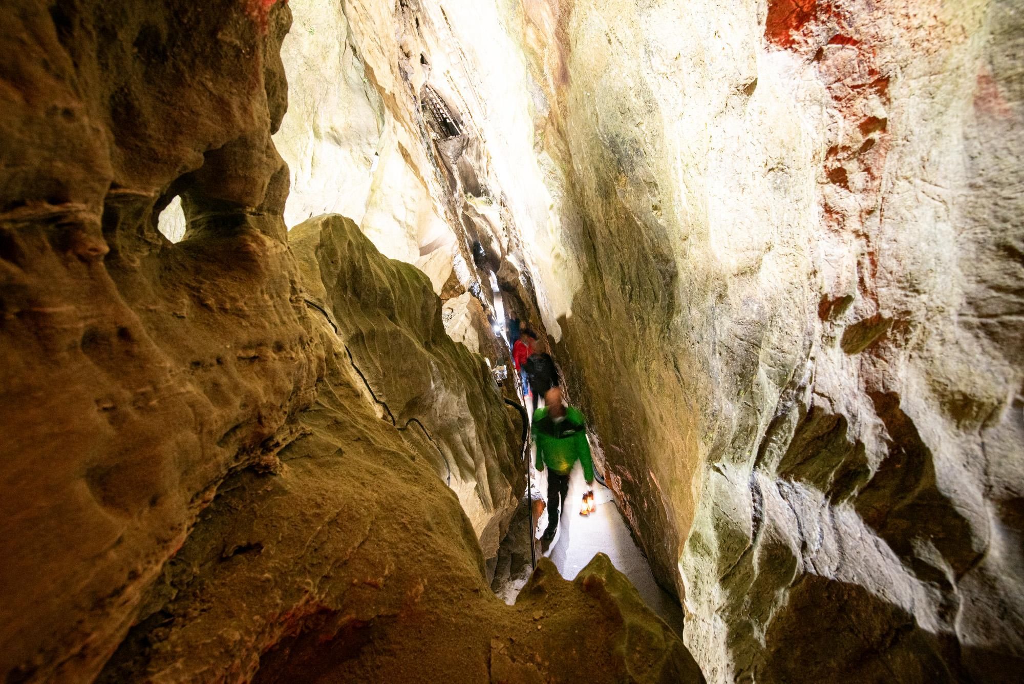 Eine Höhle mit hohen, felsigen Wänden. Wanderer bewegen sich durch das beeindruckende Landschaftsbild.