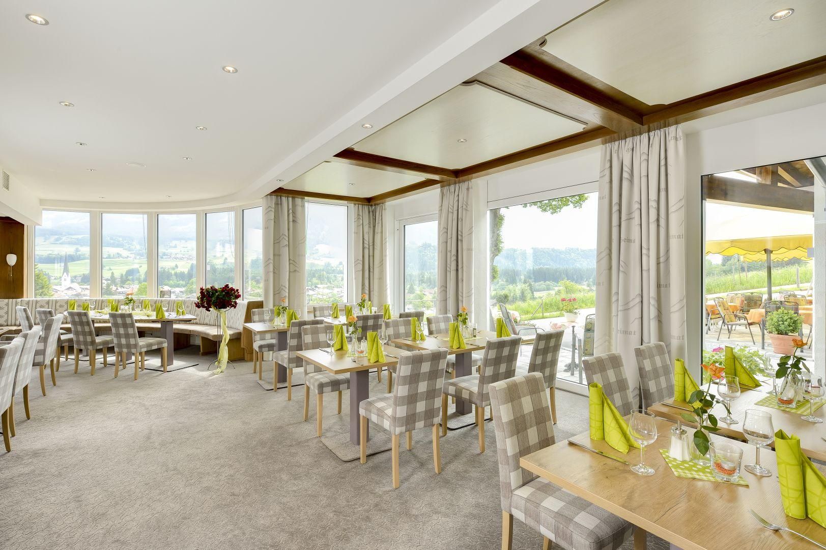 Das Restaurant im Hotel Alpenblick, ein grauer Fußboden, die Stühle sind grau-weiß kariert, viele Fenster.