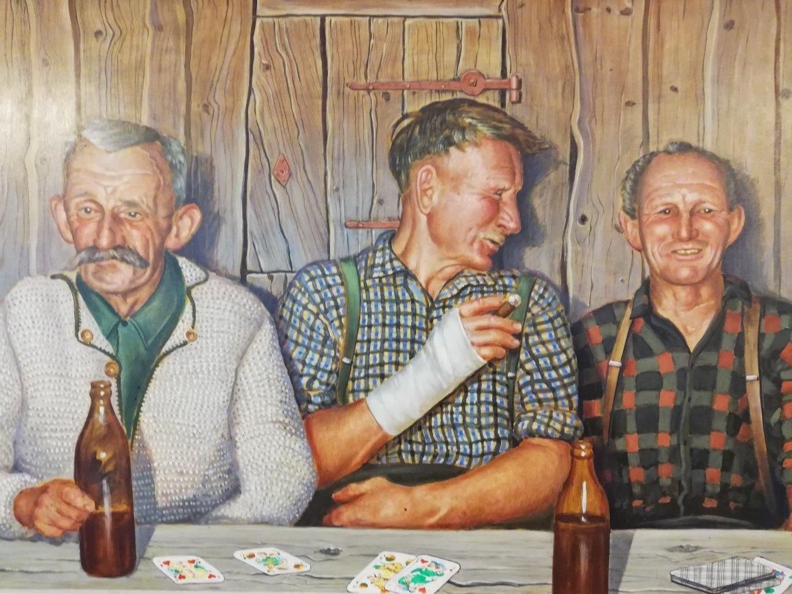 Drei lachende Männer sitzen mit Bierflaschen und Spielkarten an einem Tisch.