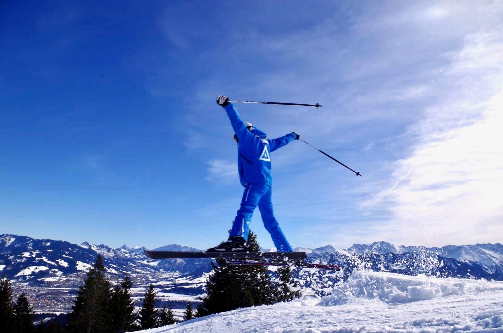 Skifahrer in blauem Anzug springt mit Skiern und Stöcken in der Luft.