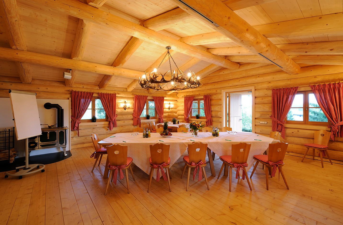 Traditionelles alpenländisches Blockhaus "Kleine Alm" im Sonnenalp Resort. Tafel für 12 Personen in der Raummitte. Leuchter aus Hirschgeweihen an der Decke.