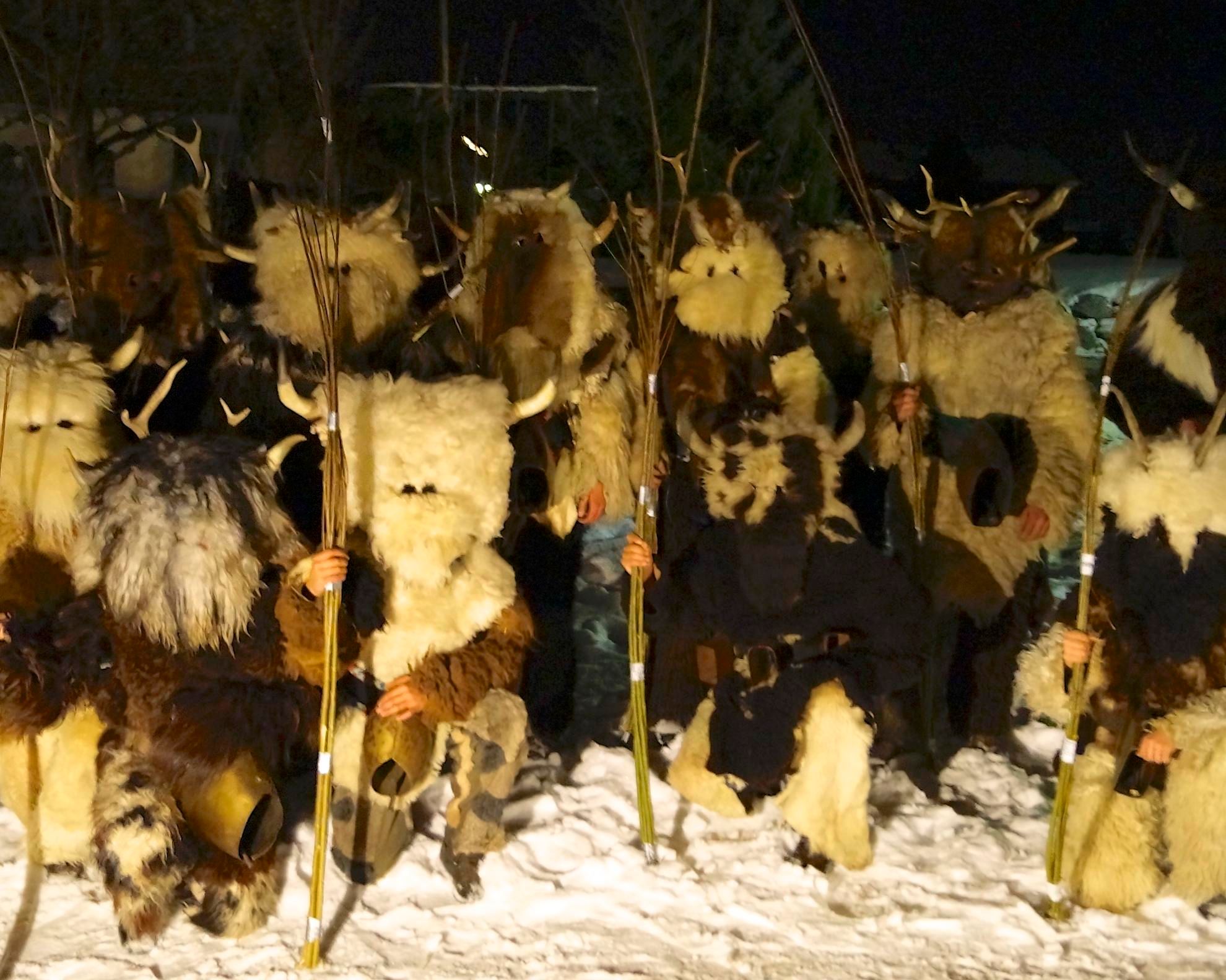 Mehrere Klausen in zotteligen Fellkostümen und Masken stehen nachts im Schnee mit Ruten.