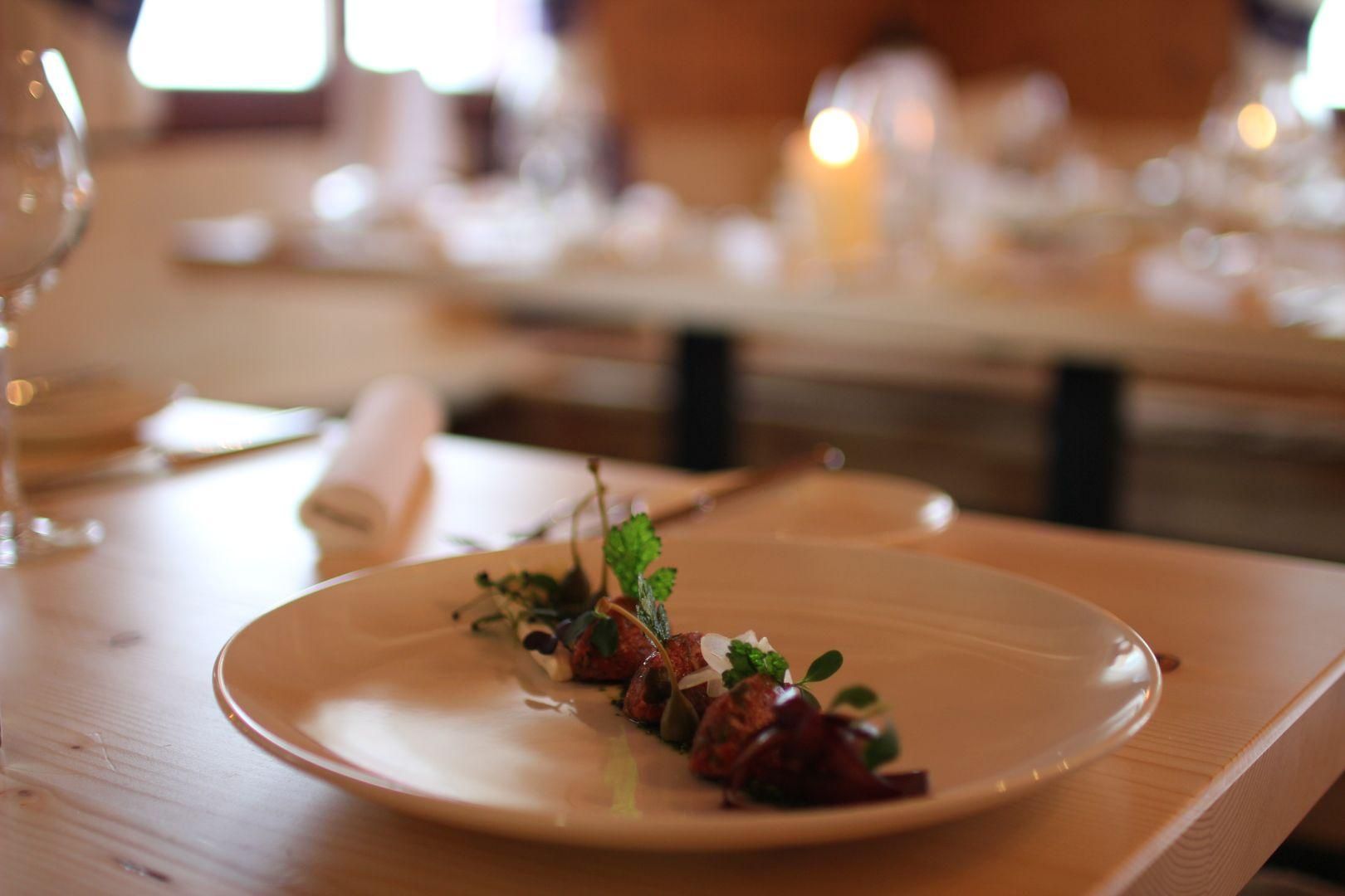 Fein angerichtetes Gericht auf einem hellen Teller in der Fuchsalm. Kleine Fleischstücke mit grünen Kräutern und weißen Akzenten.