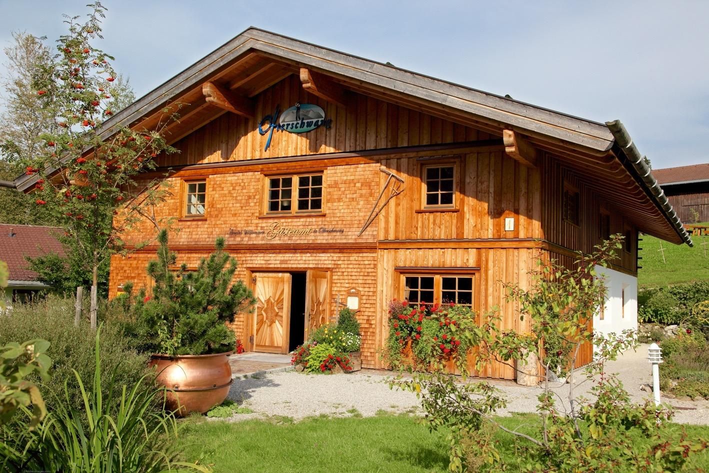 Holzhaus der Gästeinformation Ofterschwang mit Satteldach. Helle Holzverkleidung, Blumenkästen an den Fenstern.