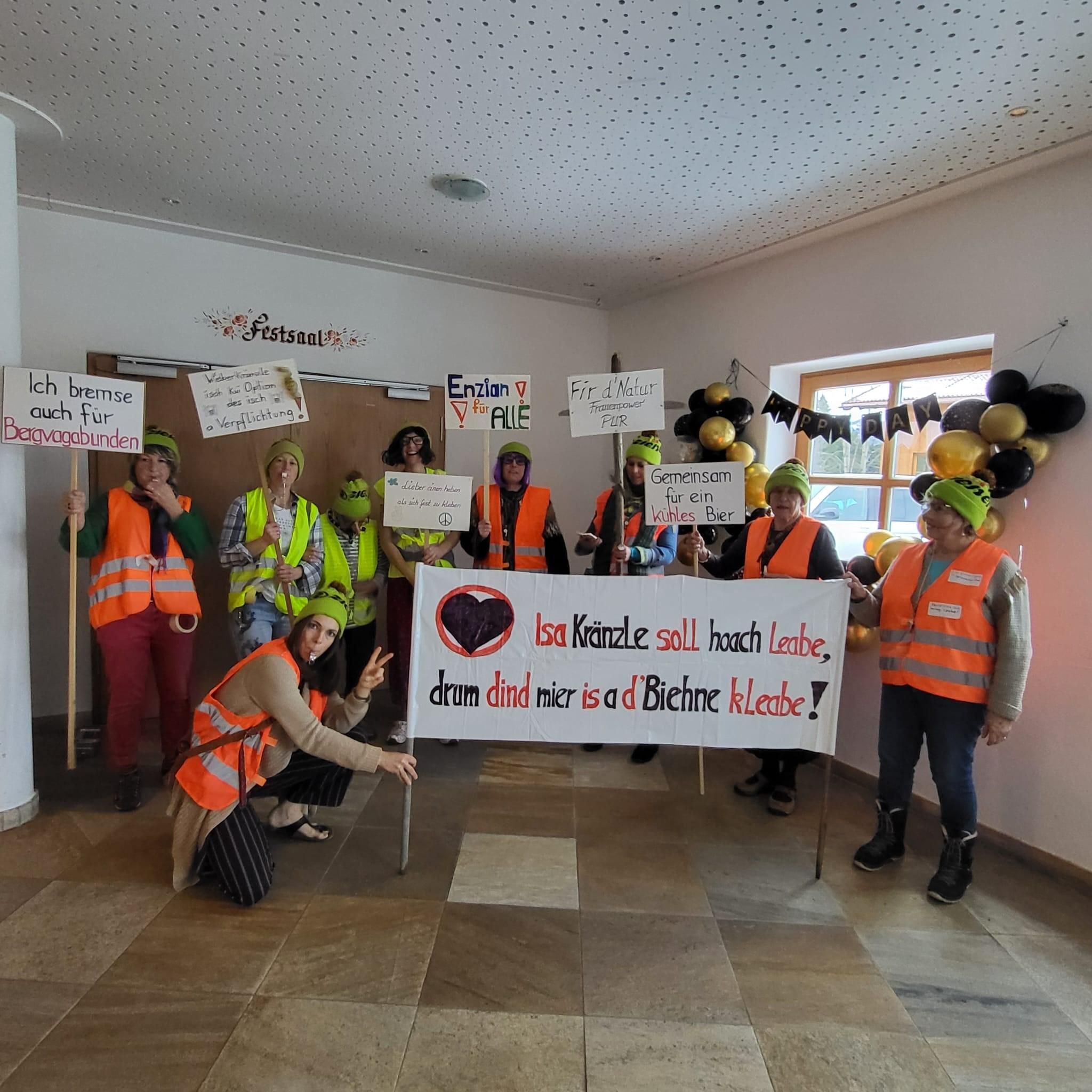Eine Gruppe von neun verkleideten Frauen hält Protestschilder und einen Banner mit lustigem Spruch über Klimakleber.
