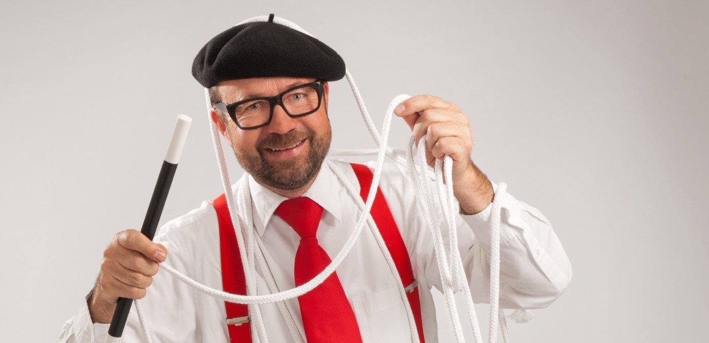 Der Zauberer Thomasius mit Zauberstab und Zauberseil, schwarze Baskenmütze, weißes Hemd, rote Krawatte und Hosenträger.