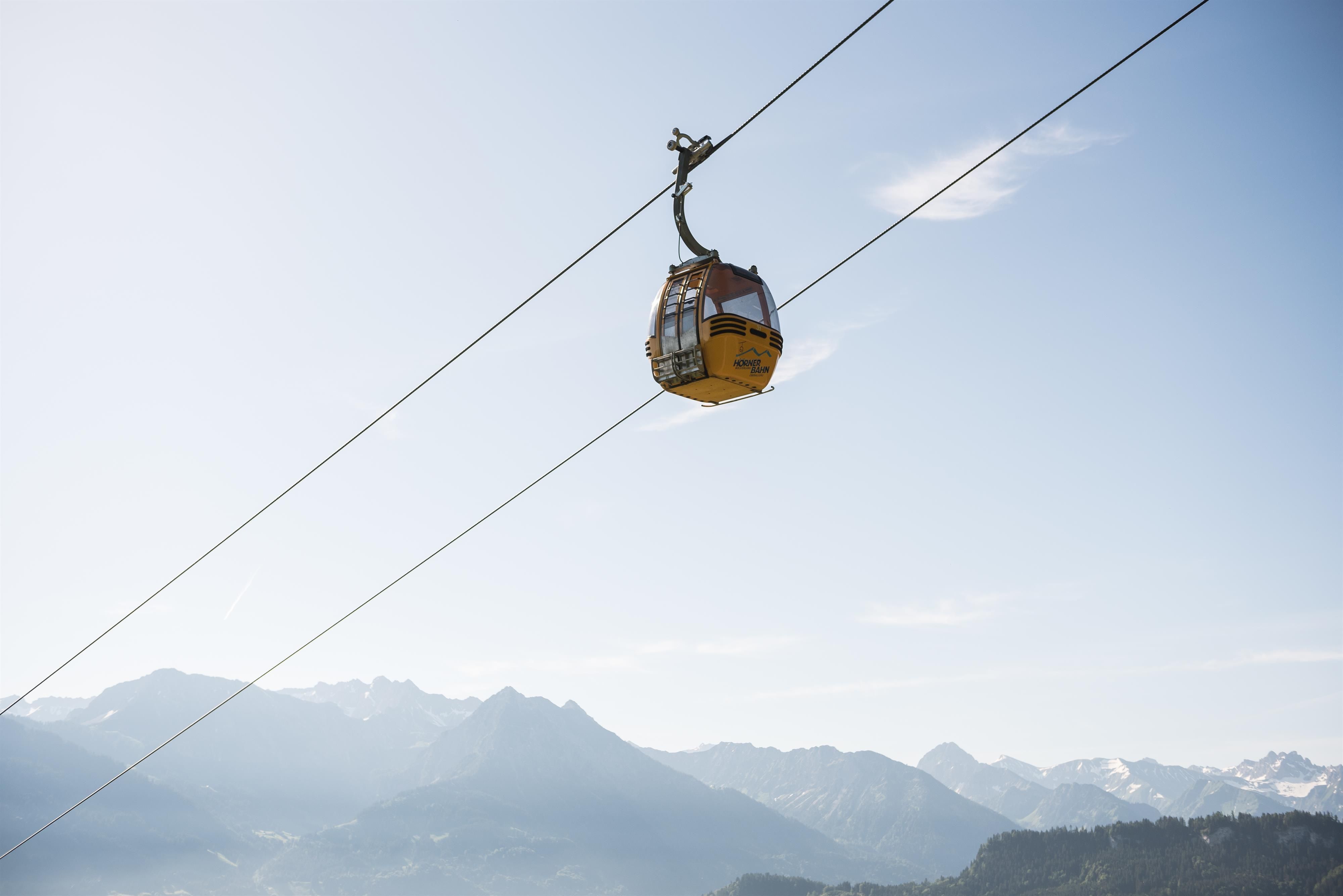 Gelbe Gondel der Hörnerbahn schwebt an Seilen über nebelverhangener Berglandschaft unter blauem Himmel.