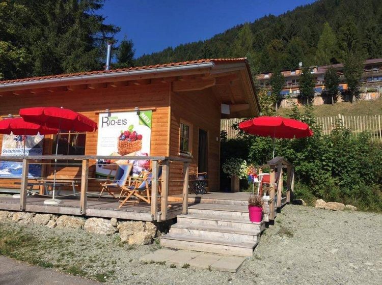 Die Biancas Bio-Eisdiele in Balderschwang ist ein kleines Holzhaus mit einer Terrasse und roten Sonnenschirmen.