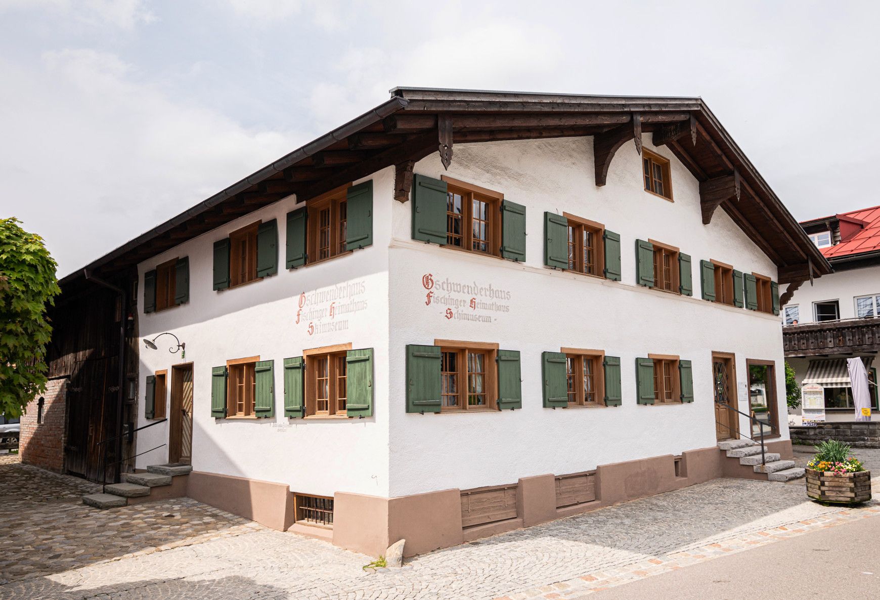 Traditionelles, zweistöckiges Heimathaus in Fischen mit grünem Dach und grünen Fensterläden. Das Haus ist weiß gestrichen.