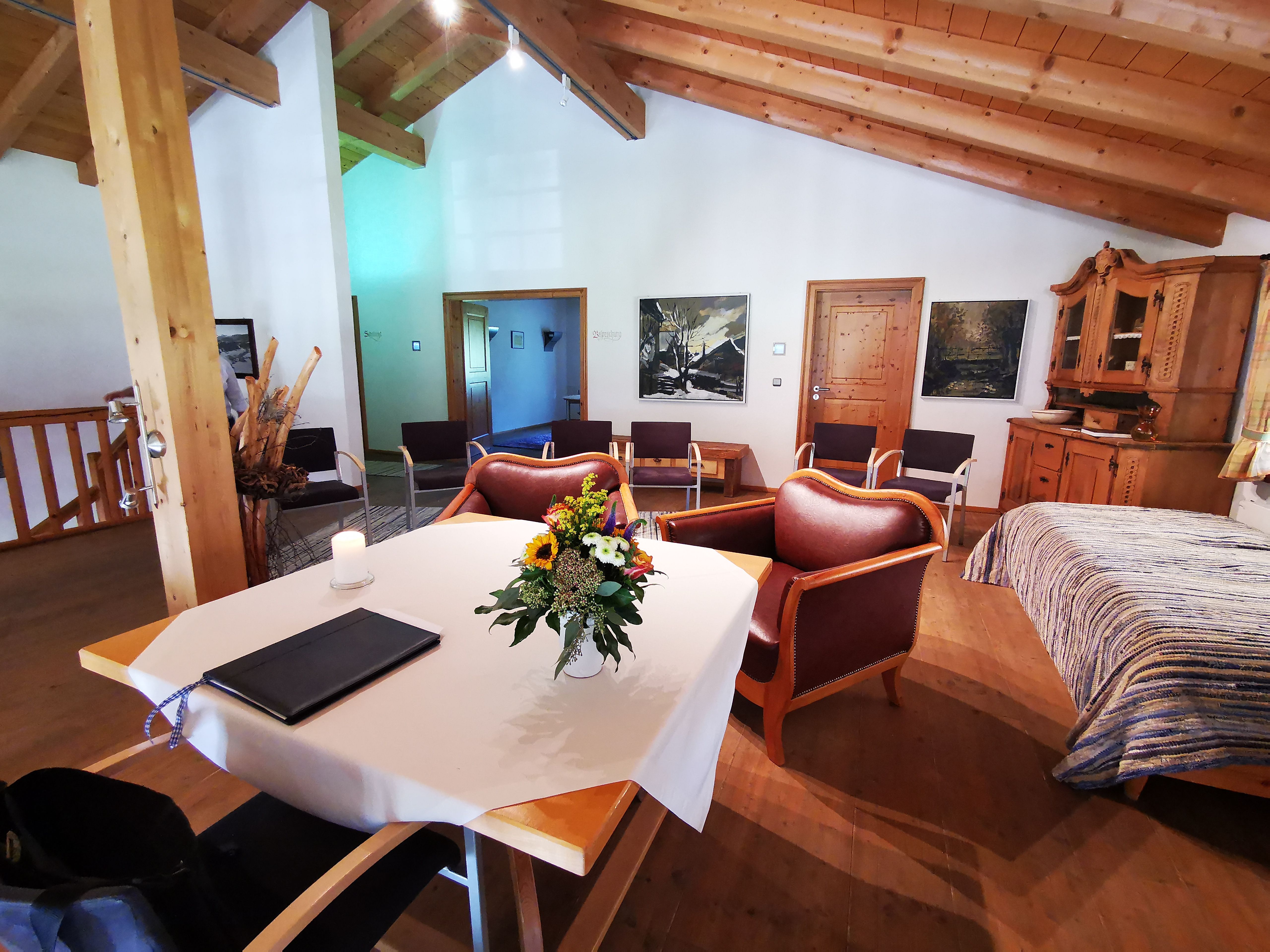 Schlicht dekorierter Trautisch auf der Galerie in der Gästeinformation Ofterschwang mit offenem Dachstuhl. Große Sessel für das Brautpaar, wenige Stühle für die Hochzeitsgäste.