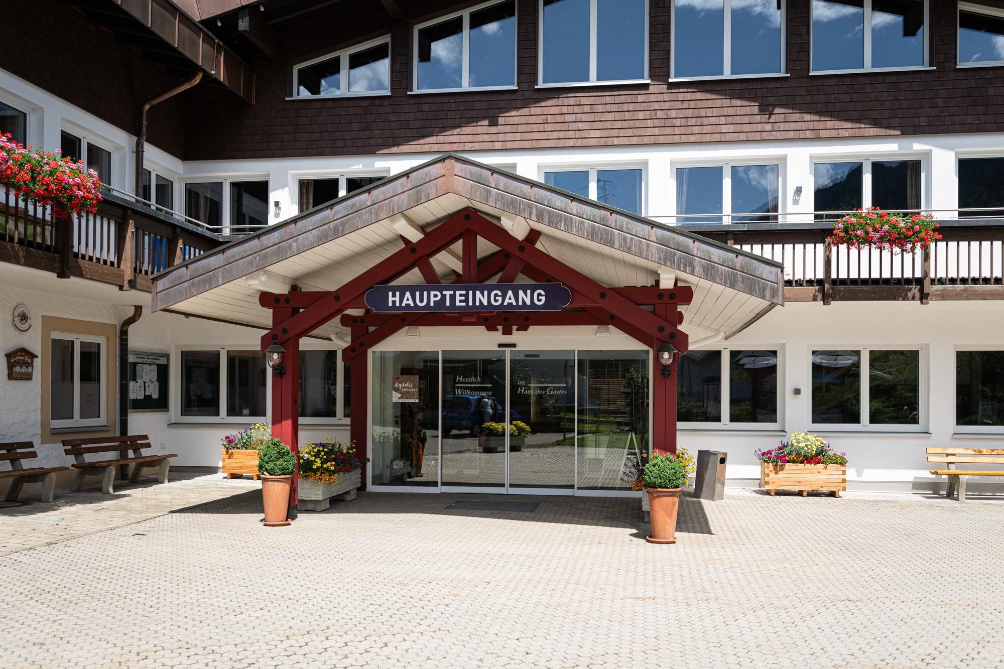 Haus des Gastes Obermaiselstein: Haupteingang mit Vordach, davor Bänke und Blumenkübel.