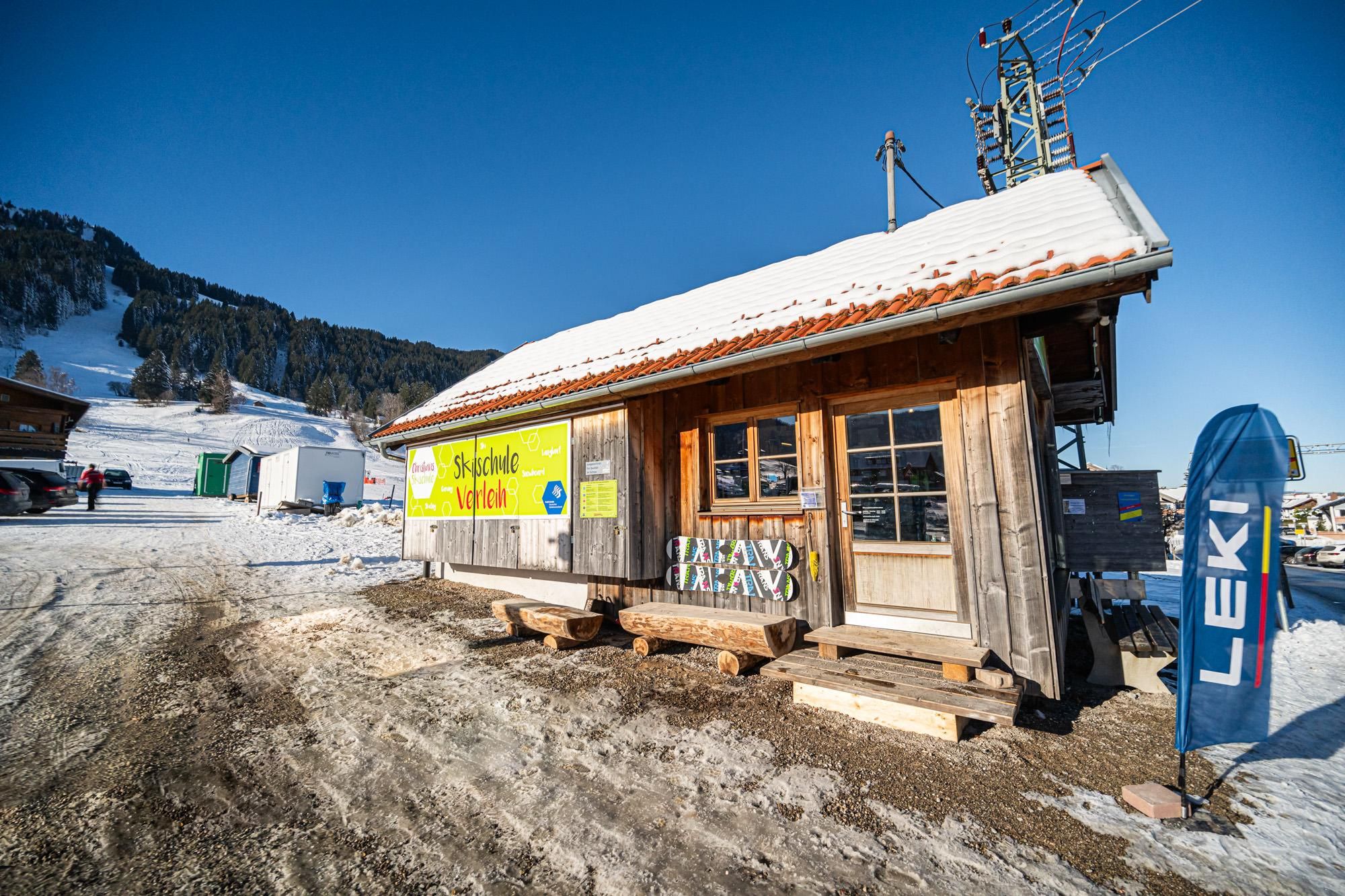 Holzhütte der Skischulel mit gelbem Schild.