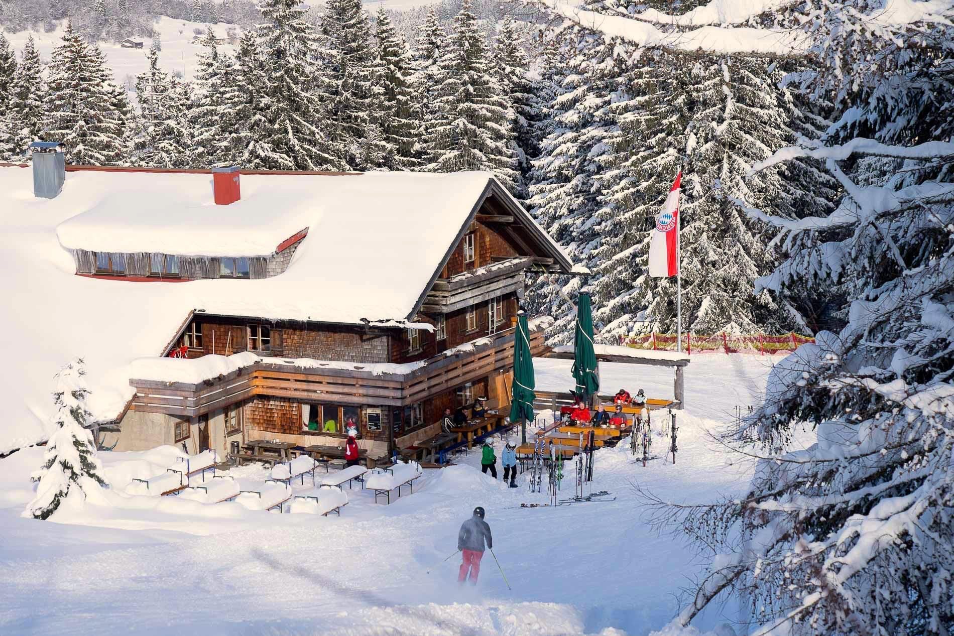 Alpe Blässe in Gunzesried im Winter, verschneite Berghütte mit Skifahrern.