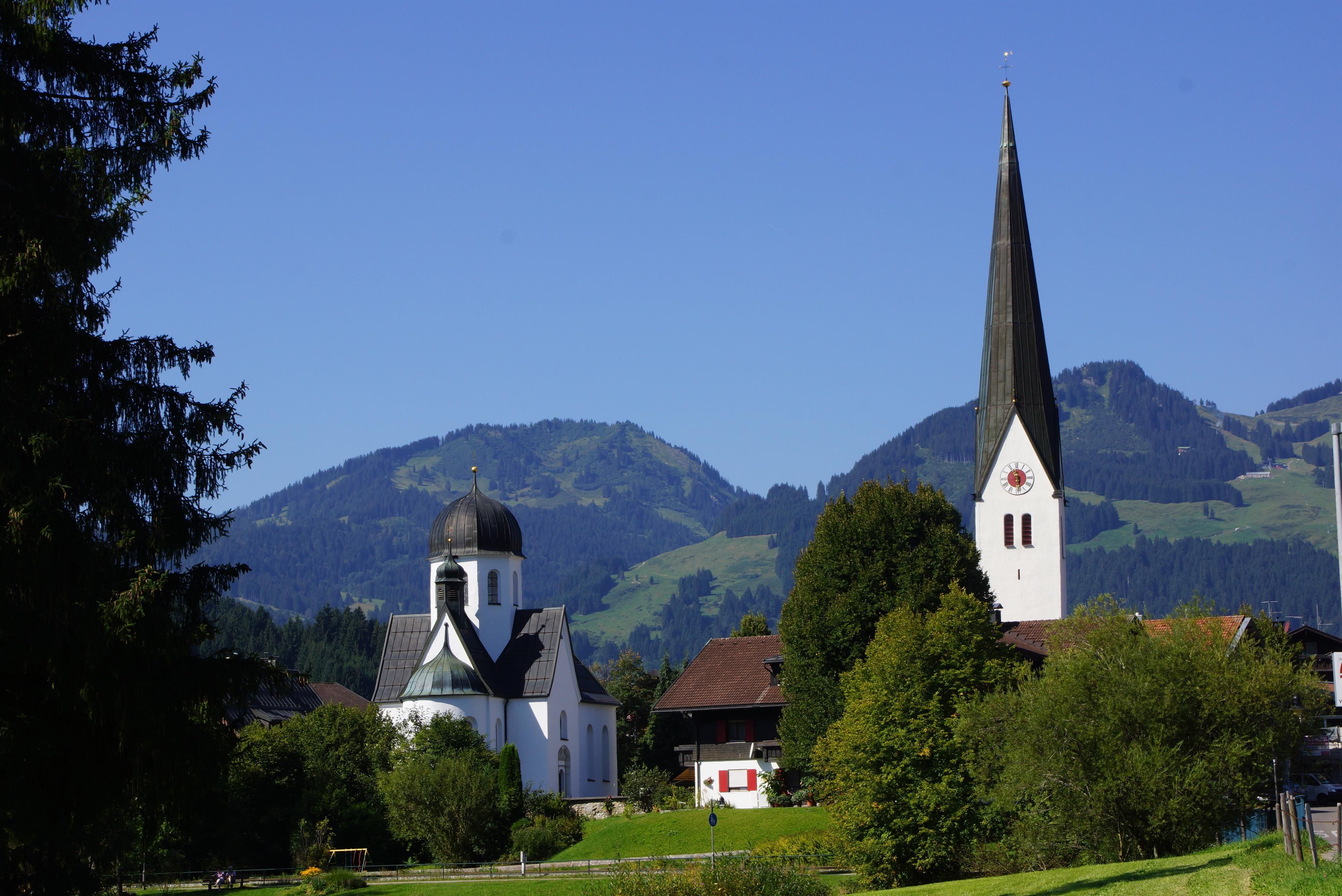 Links die Frauenkapelle, rechts die Katholische Kirche St. Verena, im Sommer, Bäume und Büsche sind dicht belaubt.