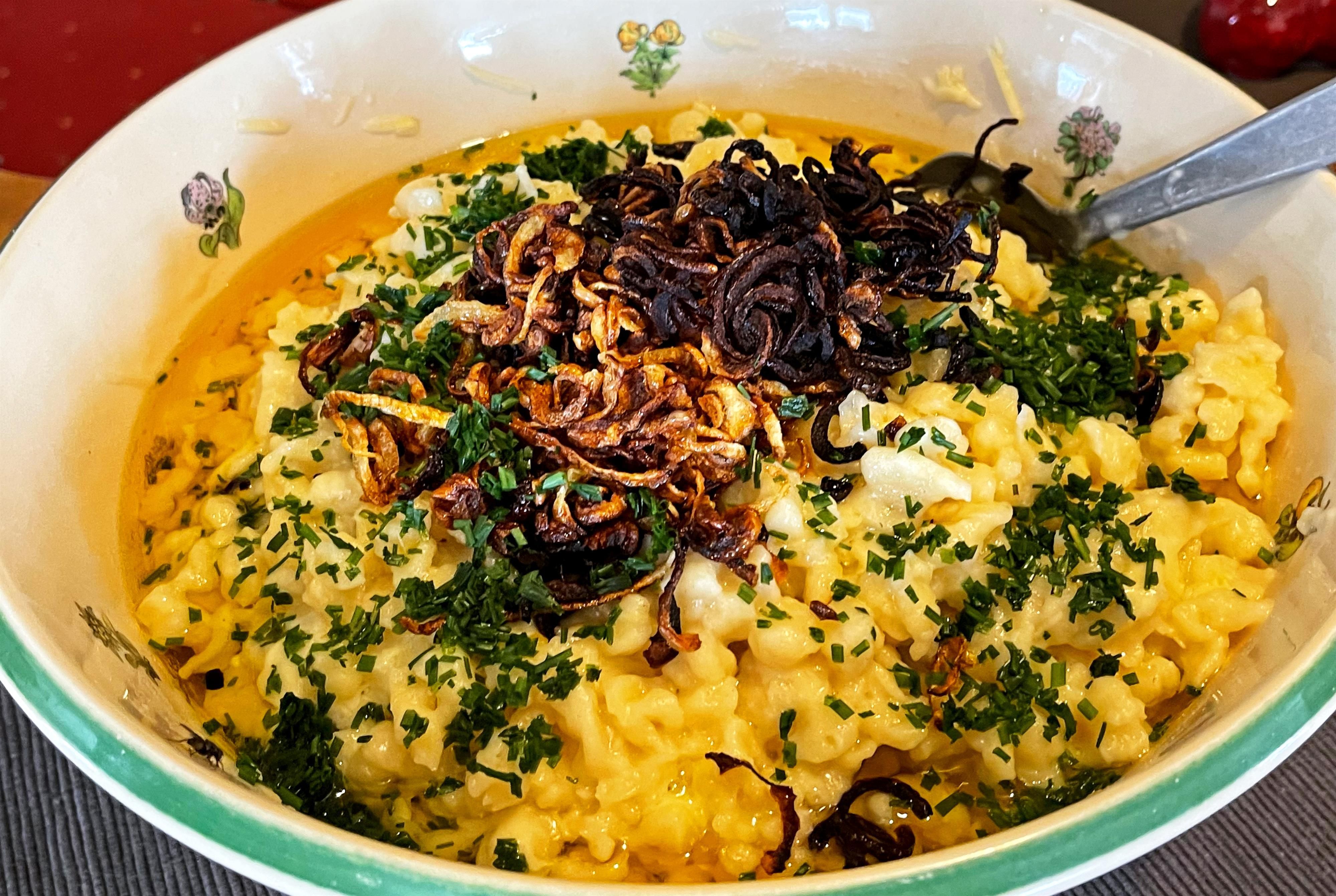 Portion Kässpatzen mit Röstzwiebeln und Schnittlauch in weißer Schale.